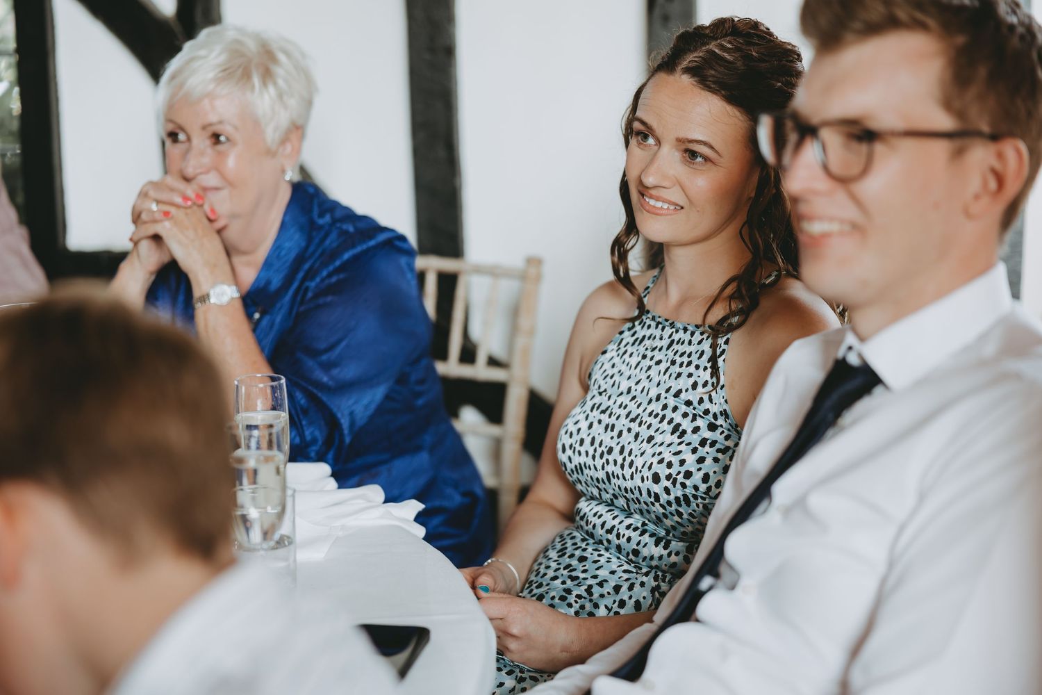 Wedding reception guests laughing and enjoying speeches at decorated banquet table.