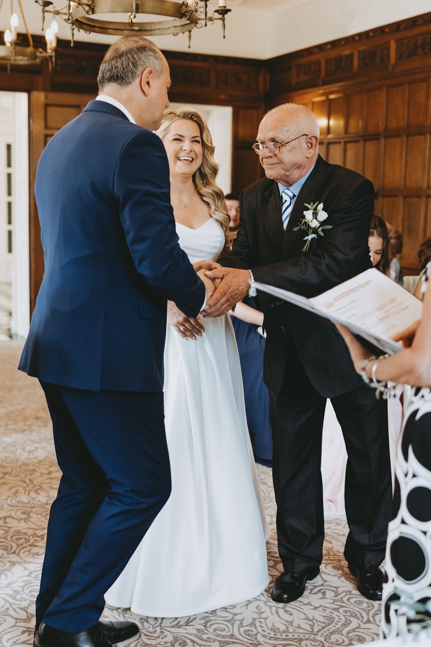 An emotional moment during a wedding ceremony in a wood-paneled room with ornate decor.