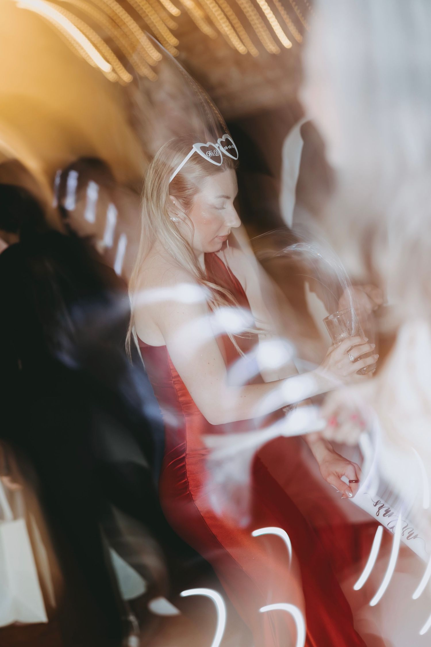 Blurred motion photo of a blonde woman in a red dress wearing a tiara at a lively party or celebration event.