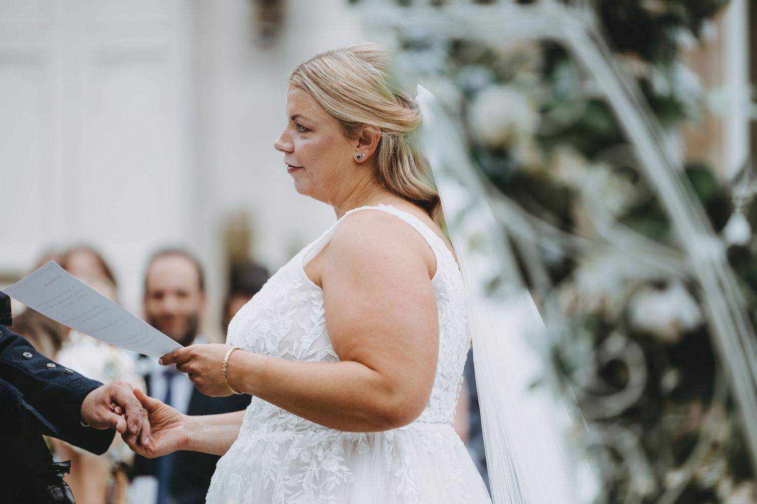 Close-up view of a wedding ceremony moment under white floral arches against stone architecture.