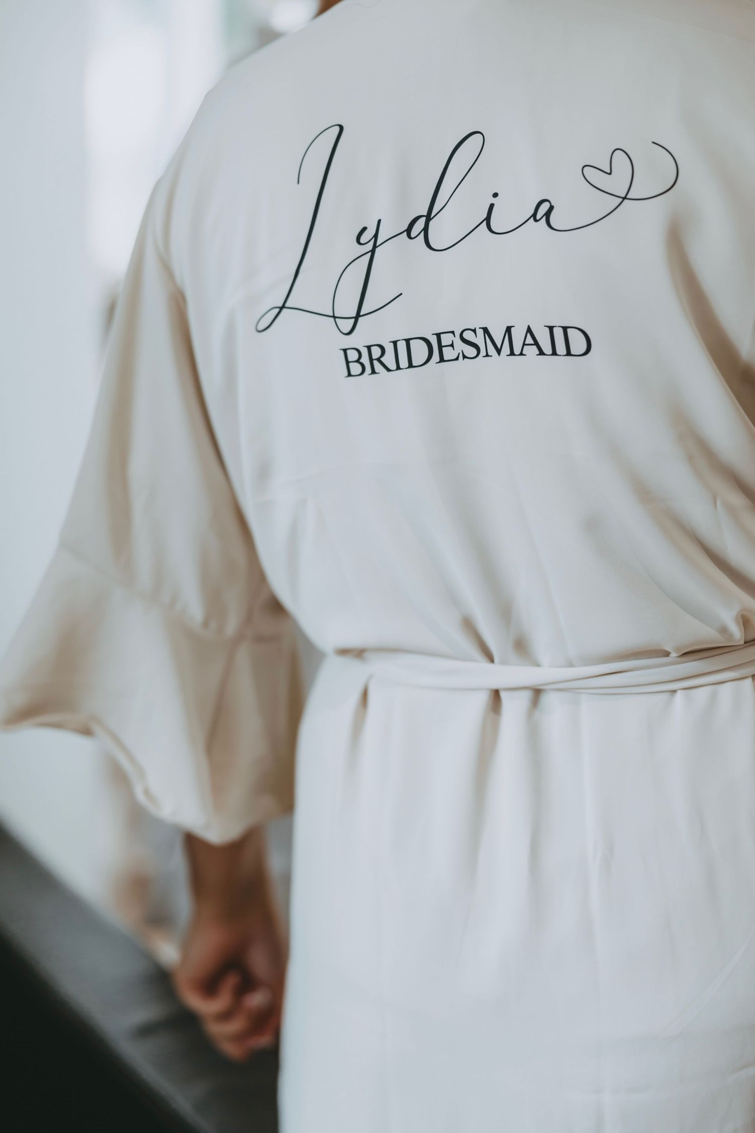 Close-up of white silk robe with 'Bridesmaid' text embroidered in elegant script.