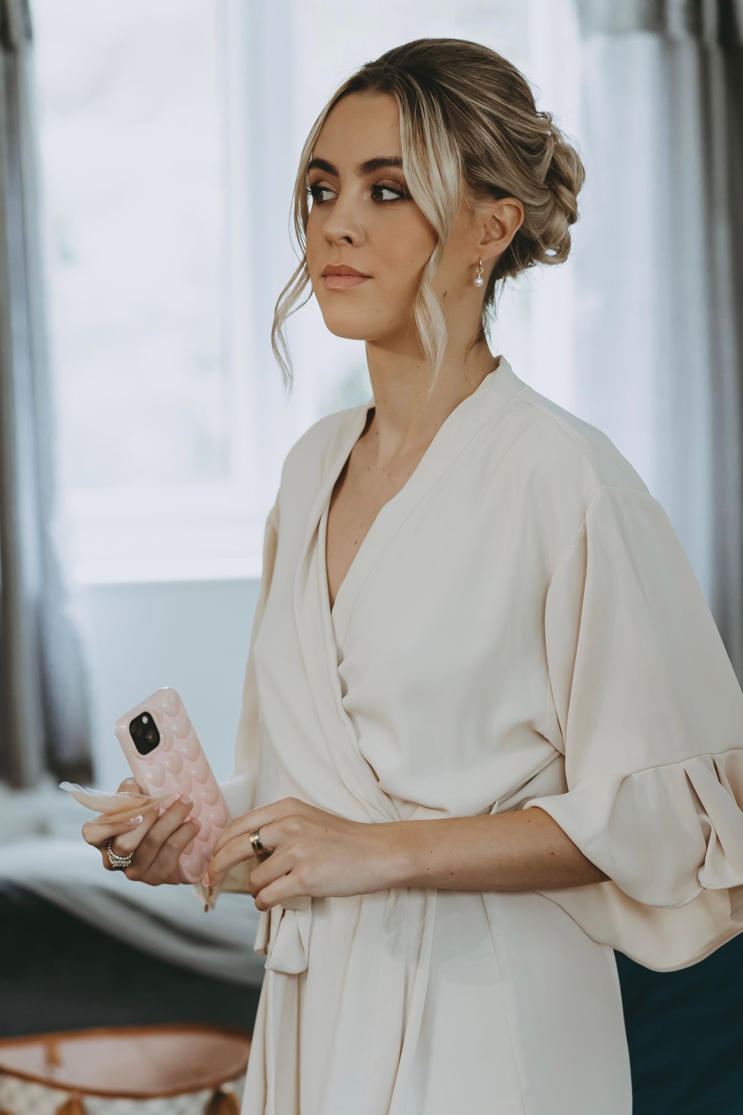 Woman in white robe checking her phone while getting ready for wedding.