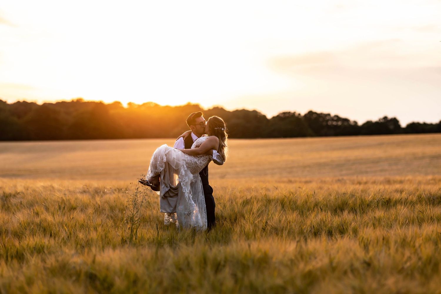 Wedding couple embraces in golden wheat field during sunset.