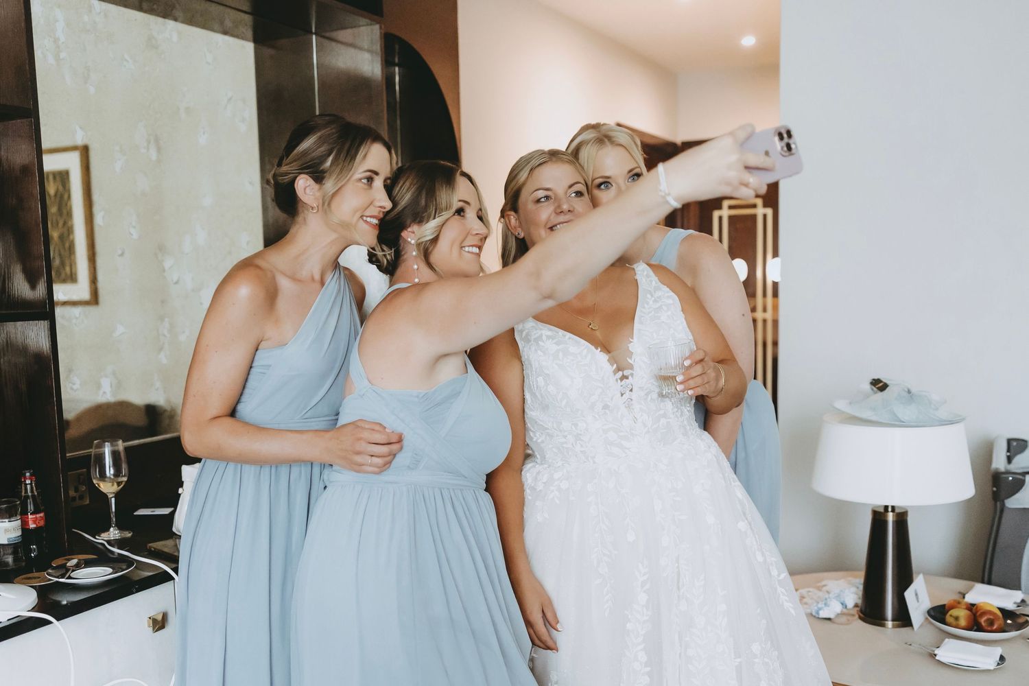 Wedding party members assist with final preparations in a modern hotel room.
