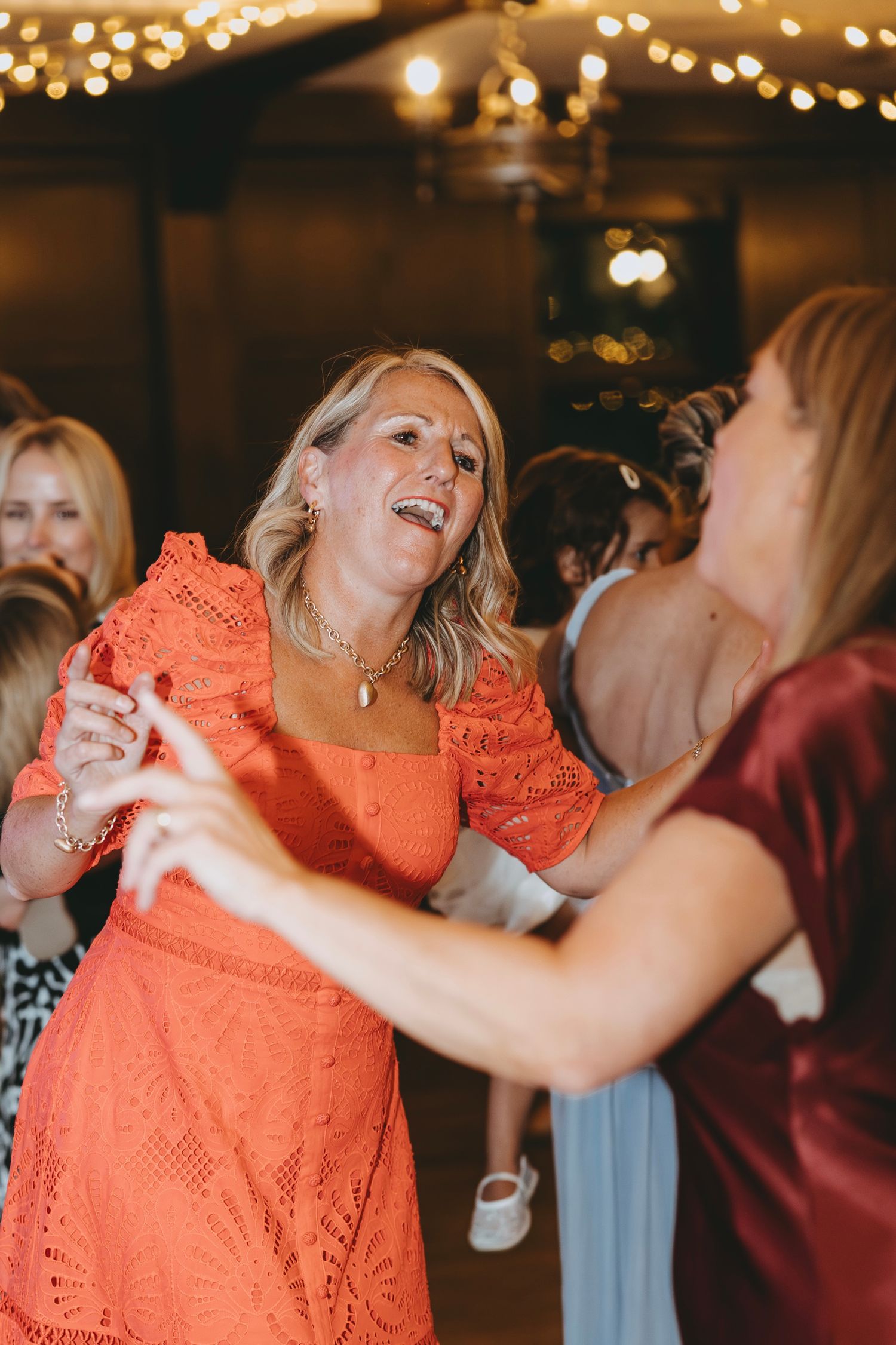 Dancers in coral lace and burgundy dresses move together under warm party lighting.