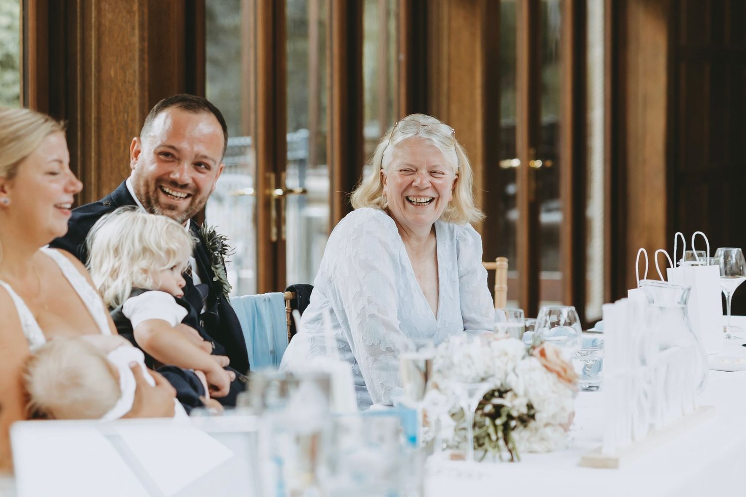 Wedding reception guests laughing and celebrating at decorated dining tables.