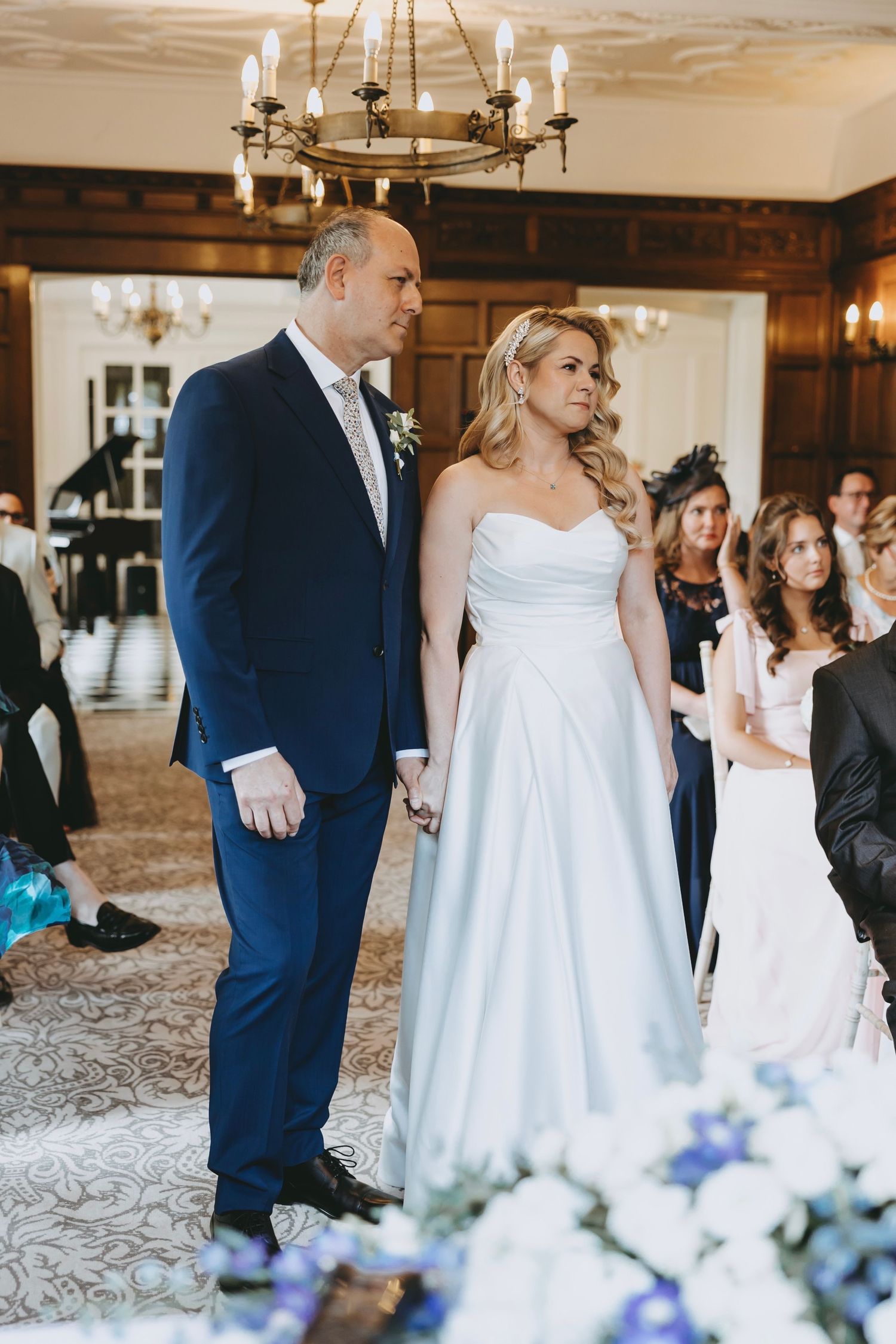 Wedding ceremony with white and blue floral decorations in an elegant wood-paneled room.