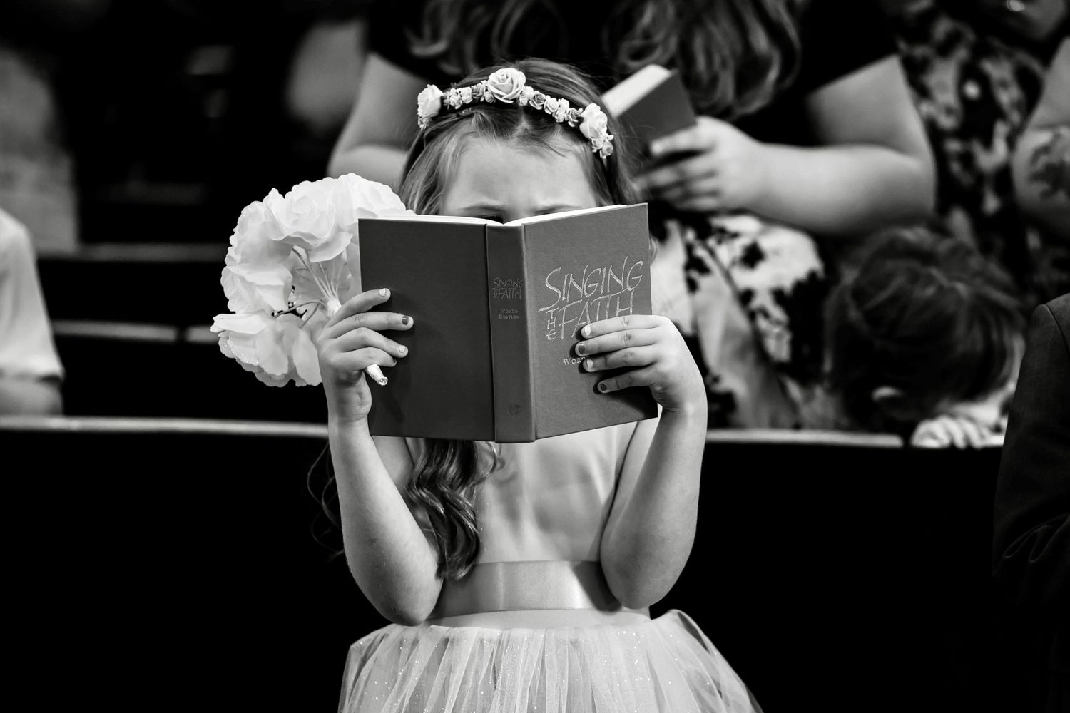 A person in formal attire reads from a book during what appears to be a wedding ceremony.
