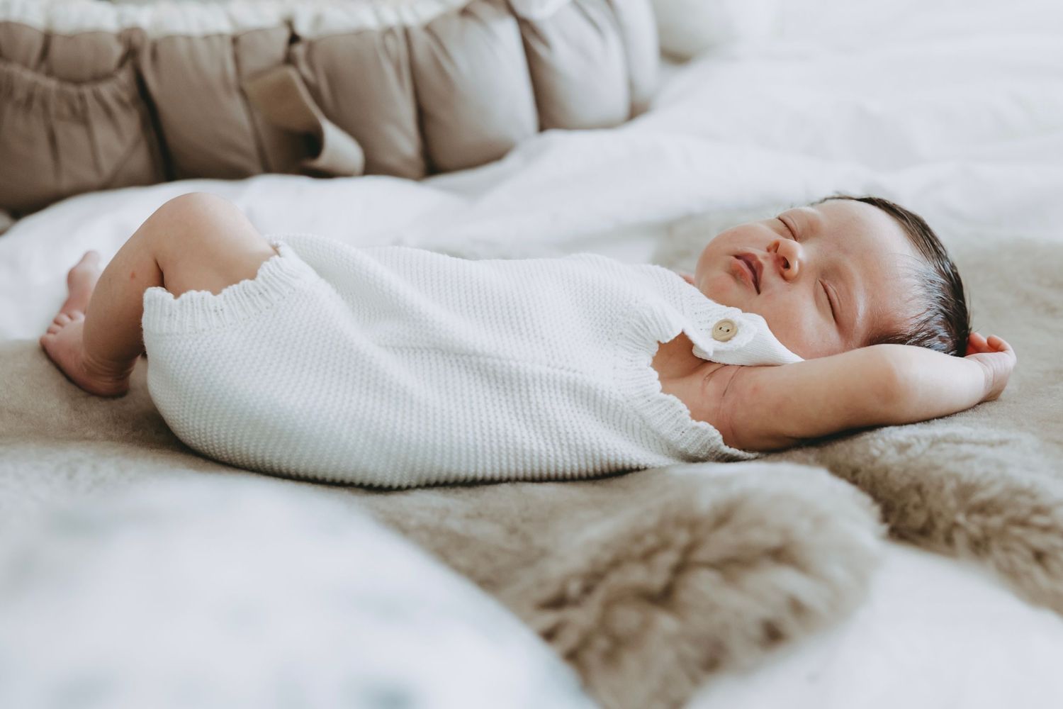 A sleeping baby rests peacefully on soft white bedding in a serene nursery setting.