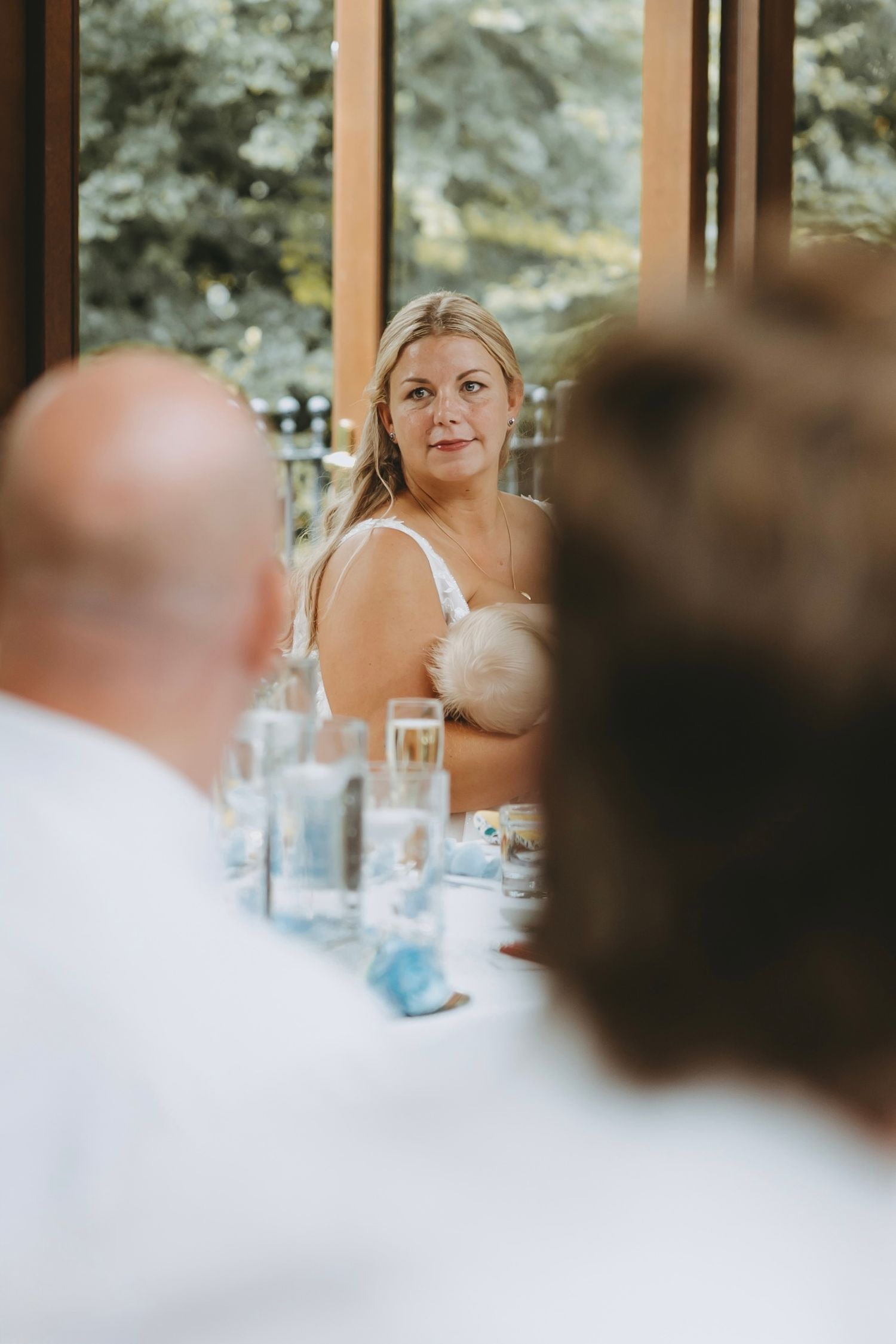 Wedding reception guests seated at tables in an elegant venue with large windows.