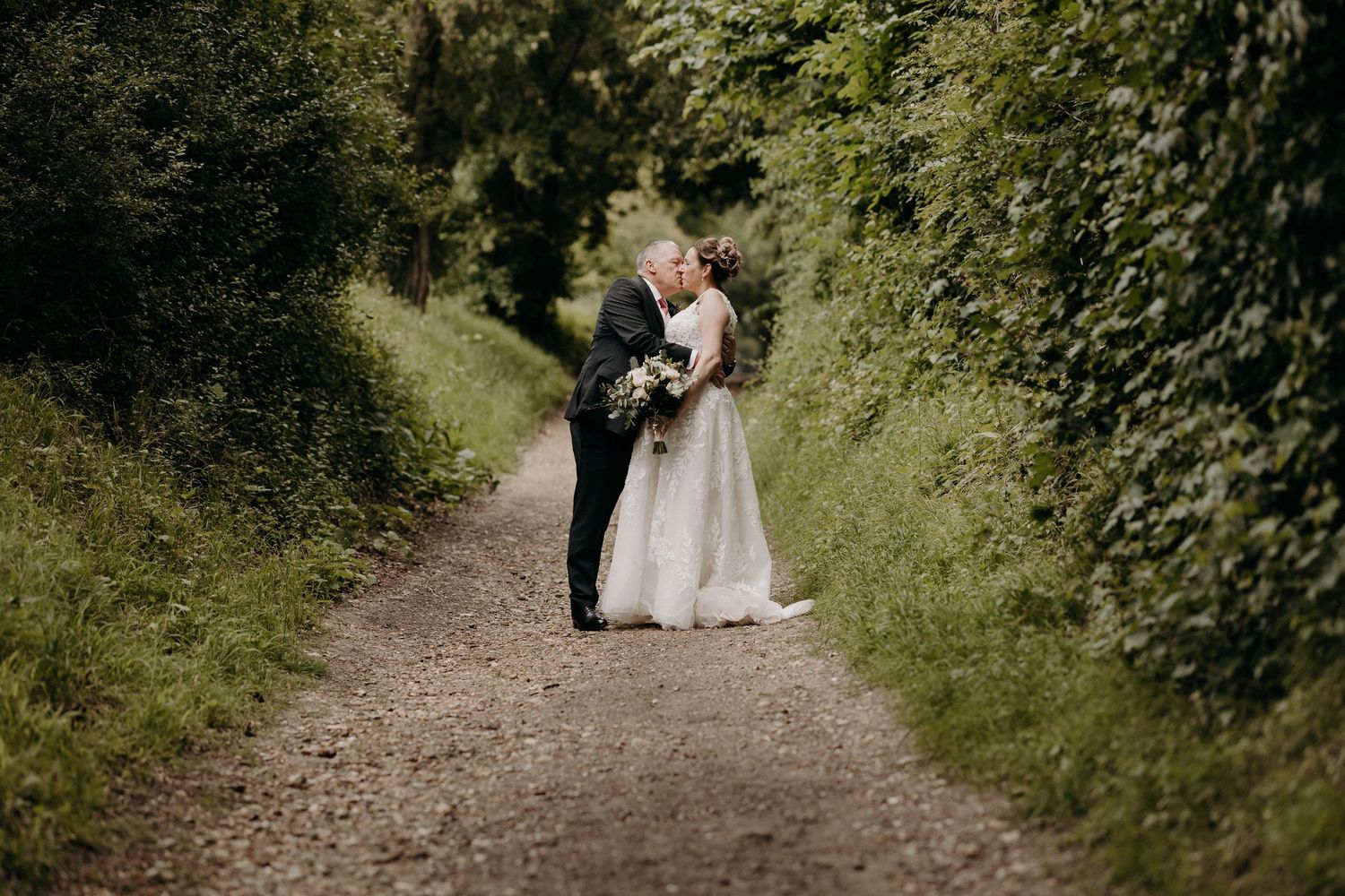 Wedding couple walking along a scenic countryside path surrounded by greenery at Tewksbury Farm, Hertfordshire.