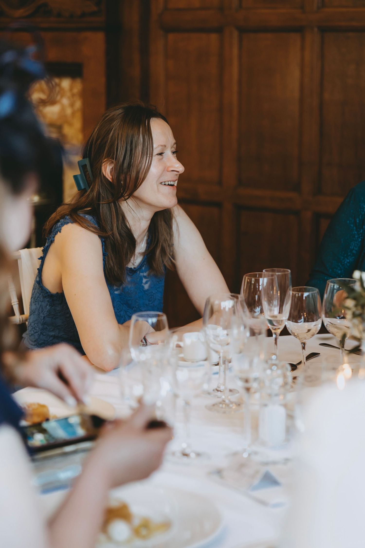 Wedding guests sharing laughs during dinner at an elegant wood-paneled reception venue.