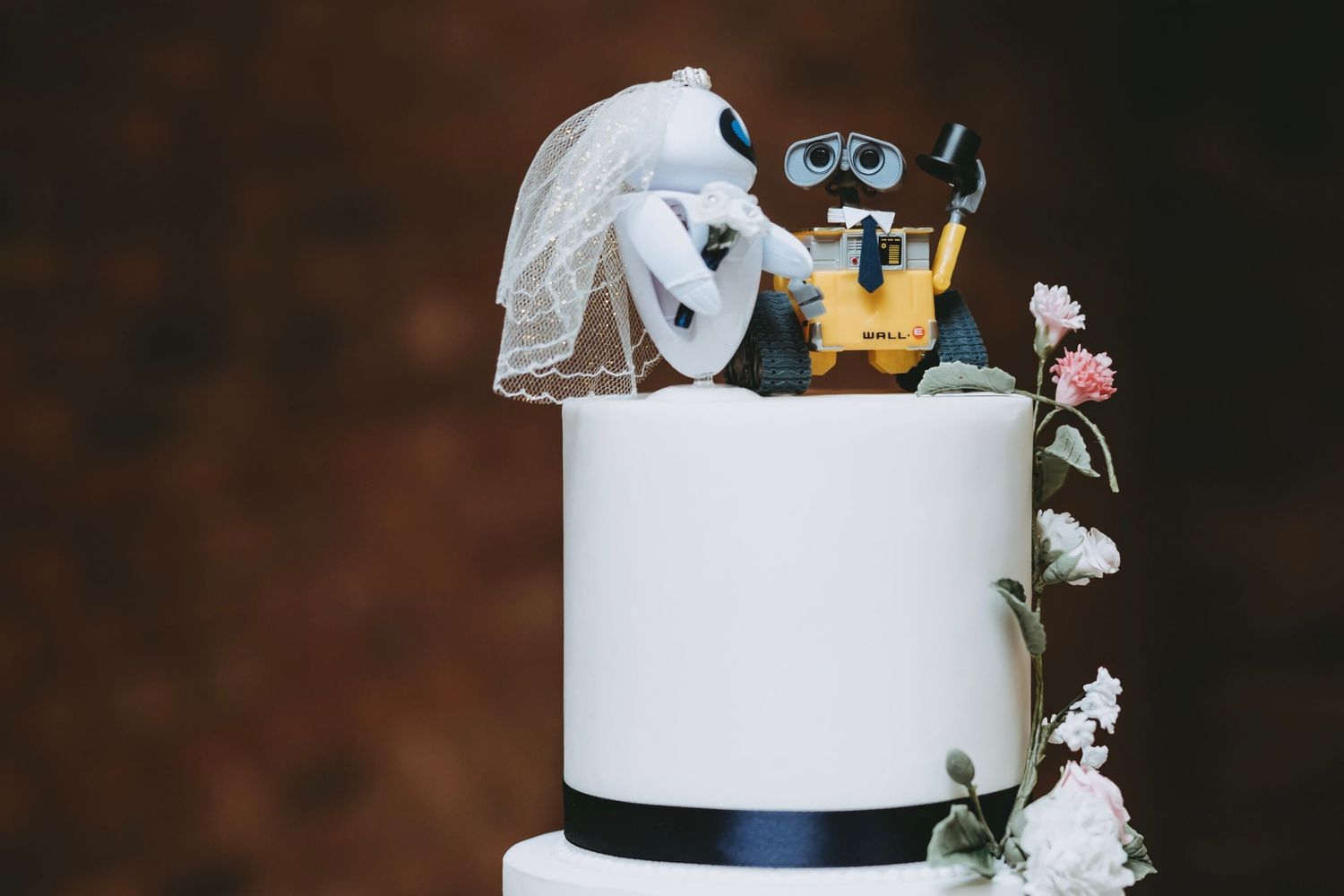 A white wedding cake decorated with metallic gold accents and white flowers sits elegantly on a dark surface.
