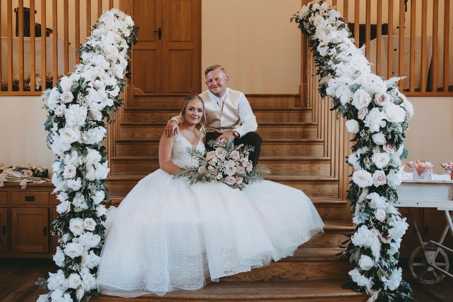 Wedding couple poses by elegant staircase decorated with cascading white flowers.