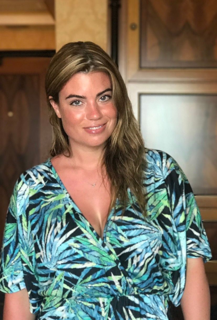 A person wearing a tropical print wrap dress with blue and green palm leaf pattern in an indoor setting.