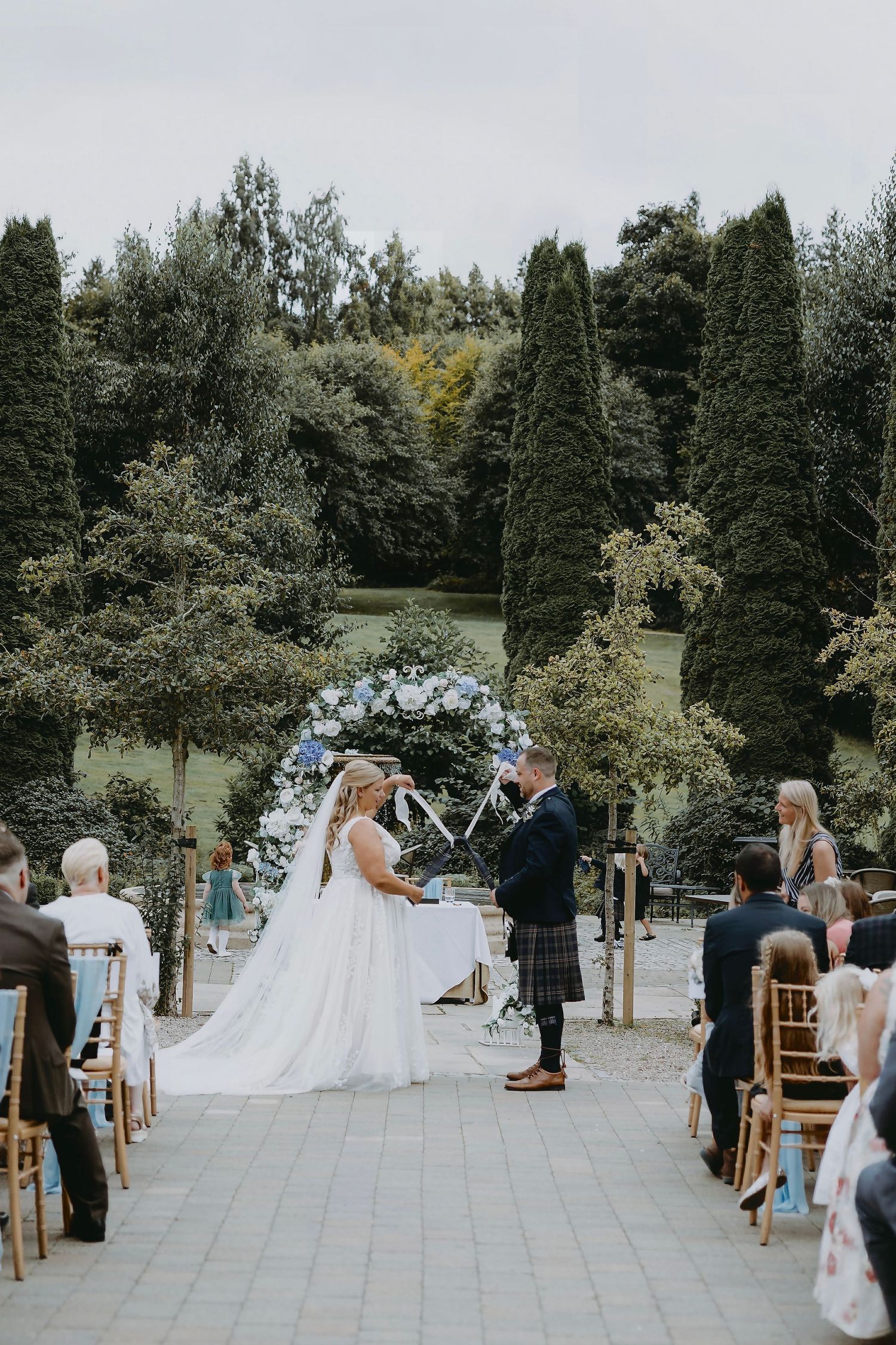Outdoor wedding ceremony setup with chairs arranged on stone patio surrounded by trees and greenery.