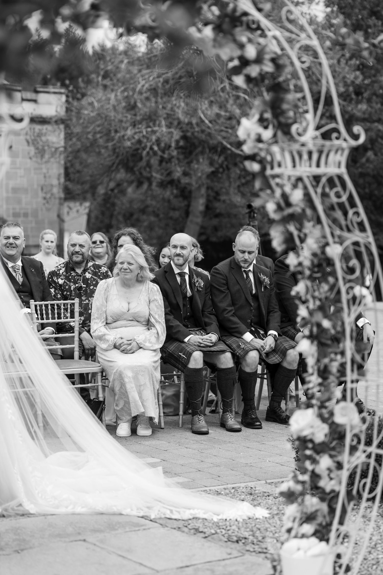 Black and white photo of wedding guests seated beneath an ornate archway.