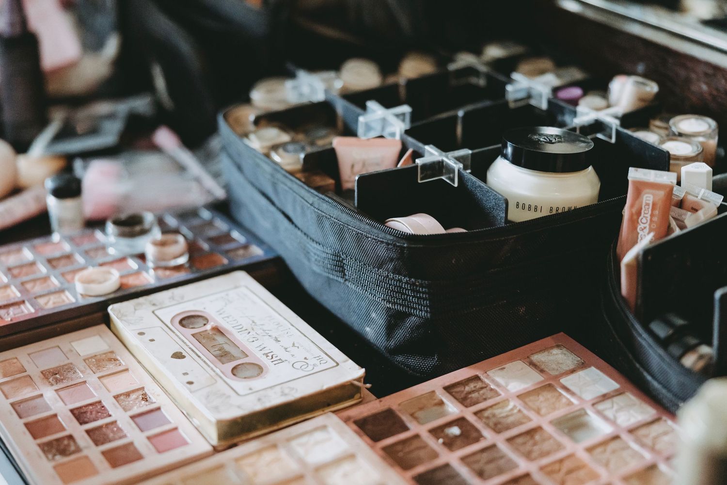 Makeup palettes and cosmetic products arranged on dark surface.
