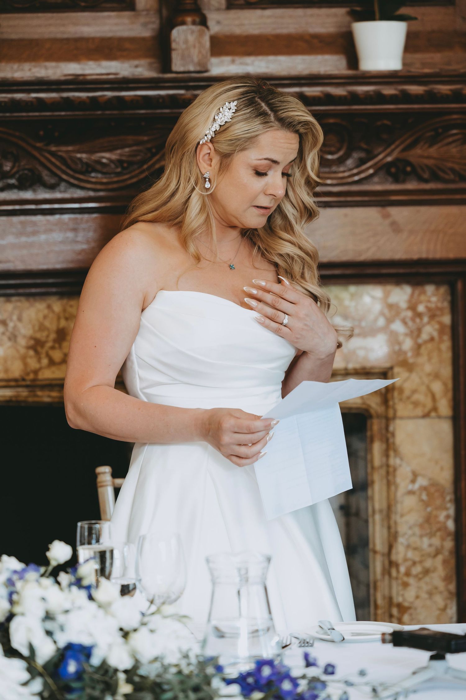 Emotional moment during wedding reception speeches with bride in white dress reading from paper.