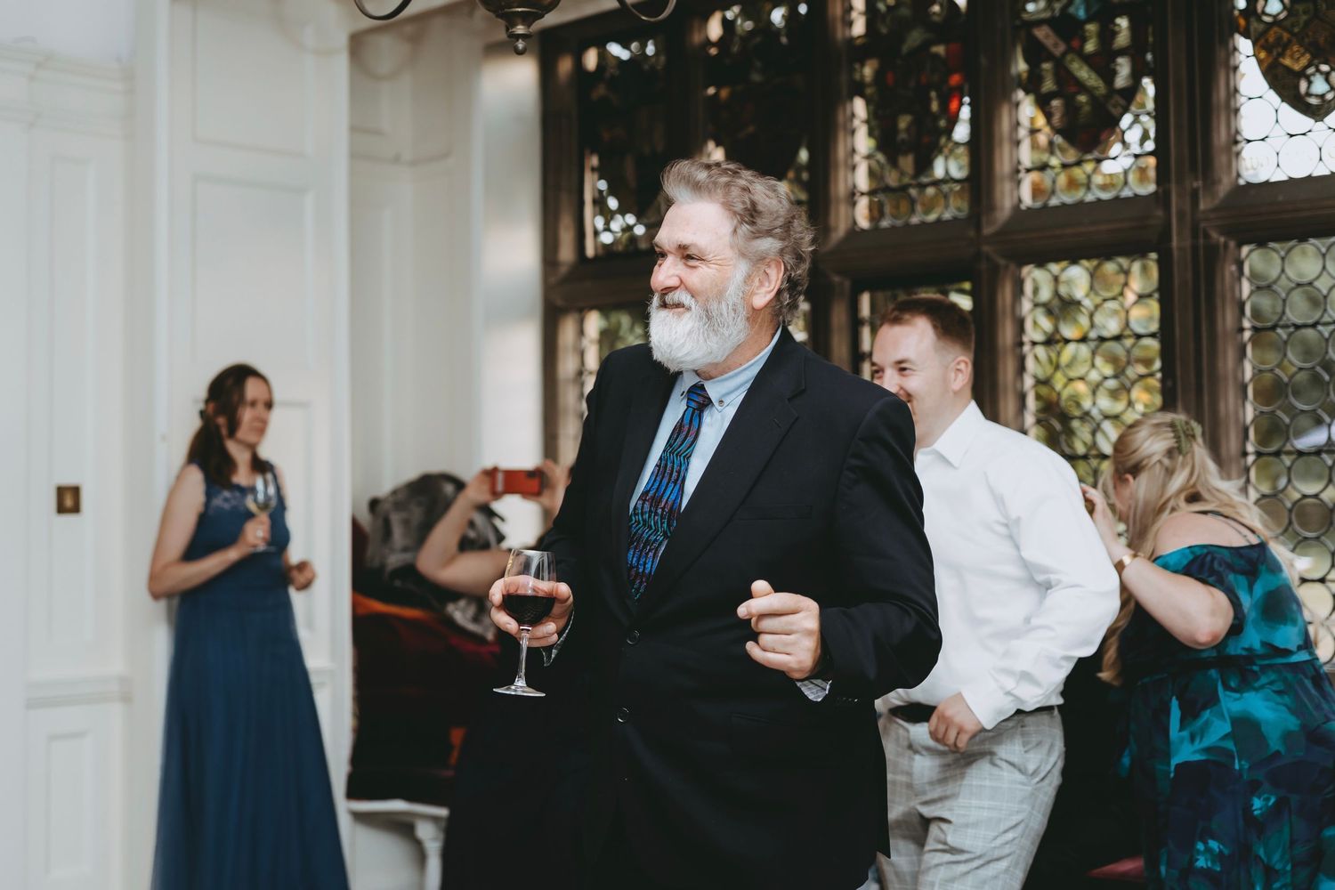 Guests enjoying drinks and conversation at an elegant wedding reception by large windows.