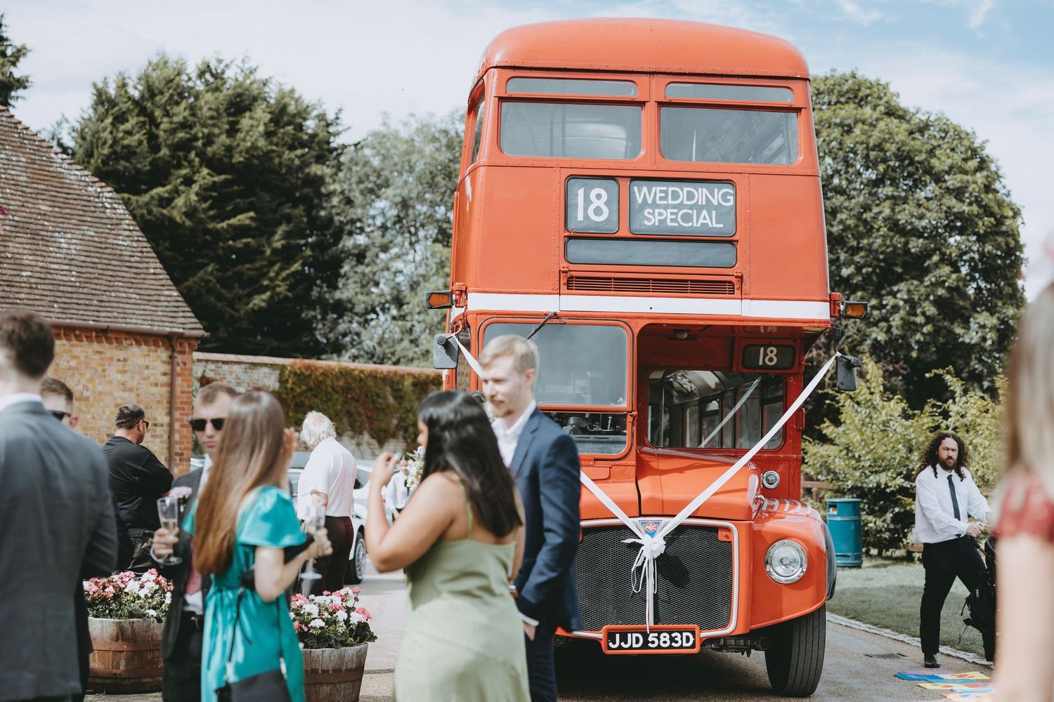 Red double decker bus parked outside on a sunny wedding day.