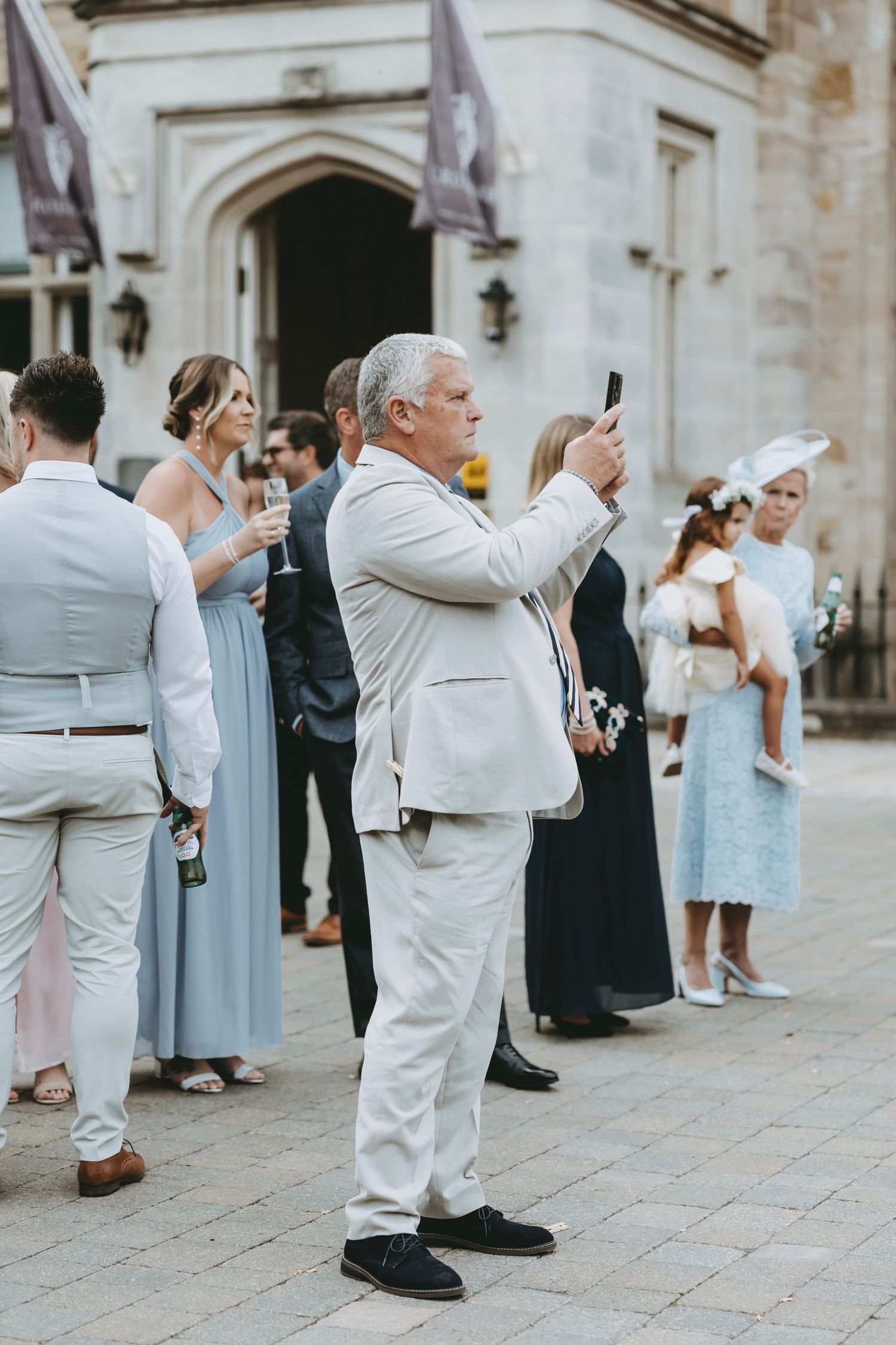 Guests in white suits take photos at outdoor wedding.