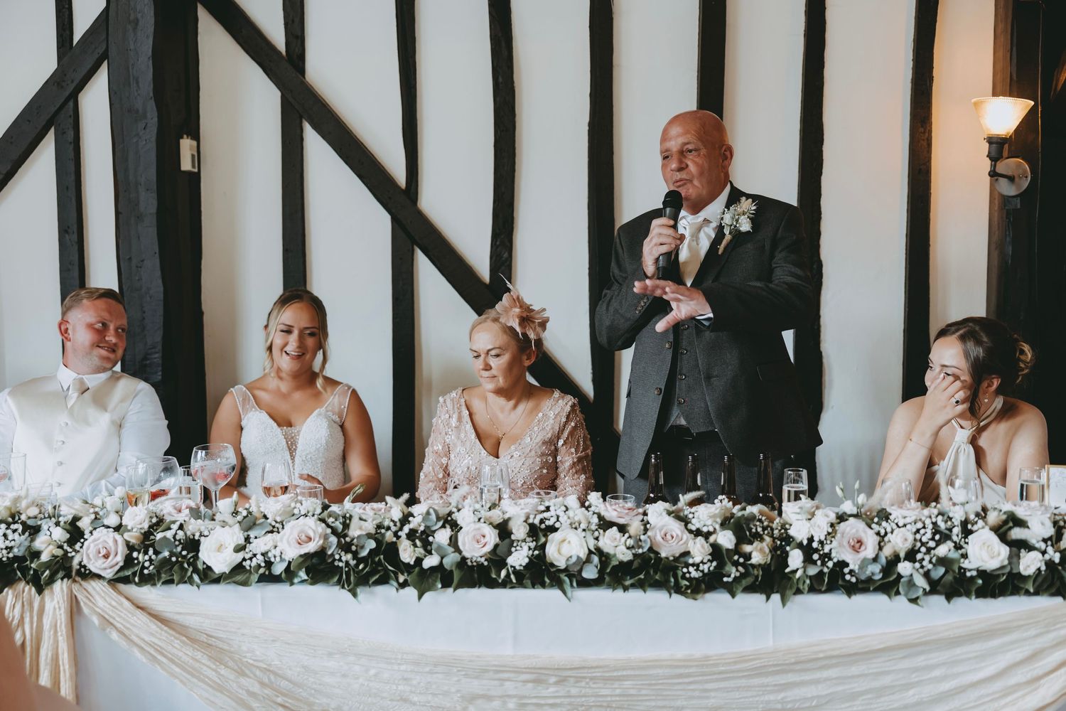 Wedding party members listening to speech at decorated head table.