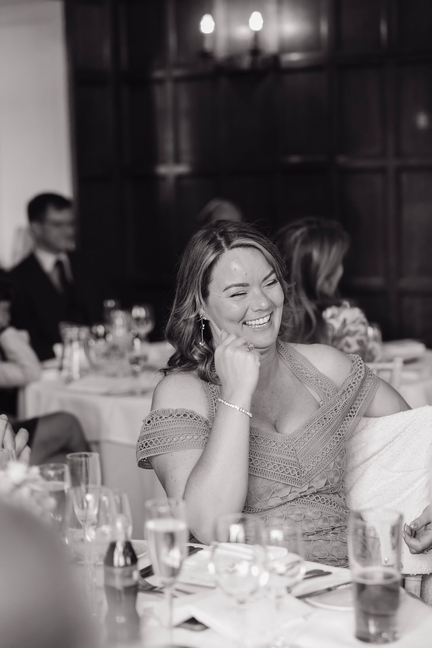 Black and white photo captures joyful reactions during wedding reception speeches.