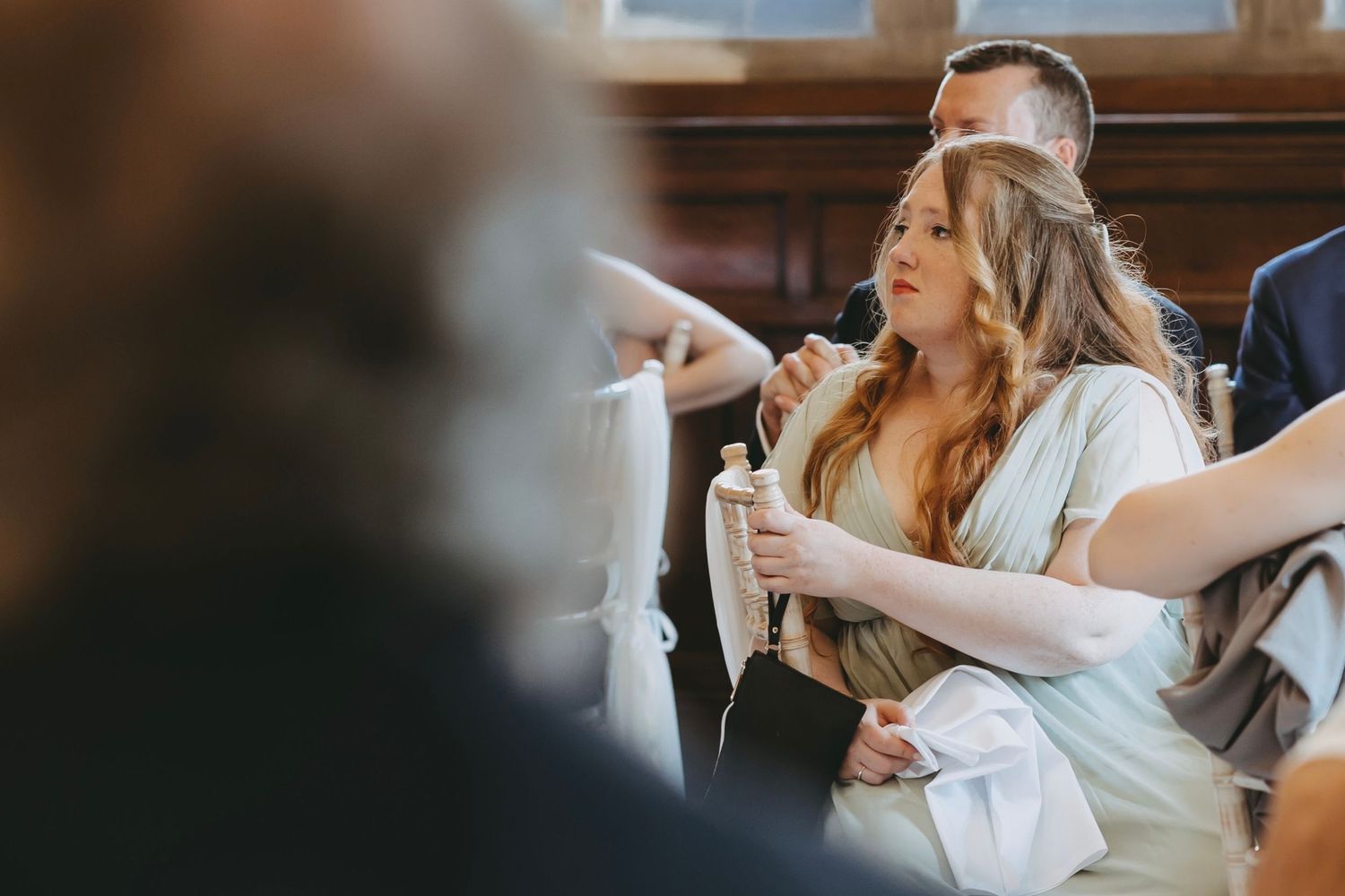 Wedding reception guests seated at long table with ornate wood paneling in background.
