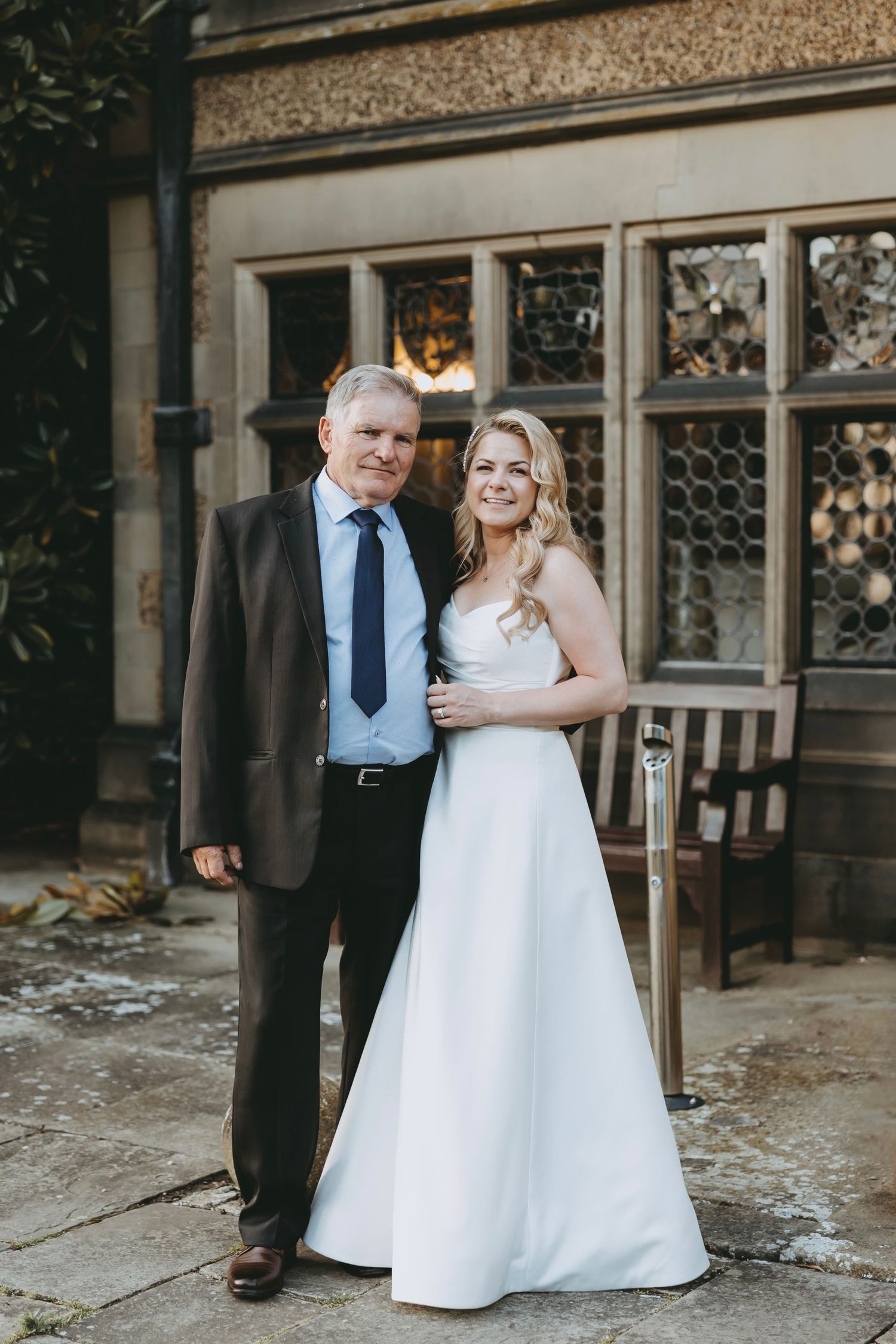 A couple poses together outdoors in formal wedding attire, with the bride wearing a white gown.