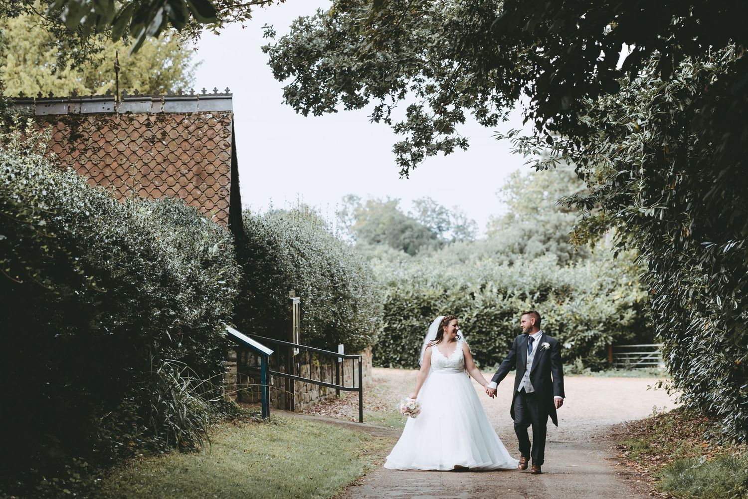 A couple walks along a garden path outside a rustic building.