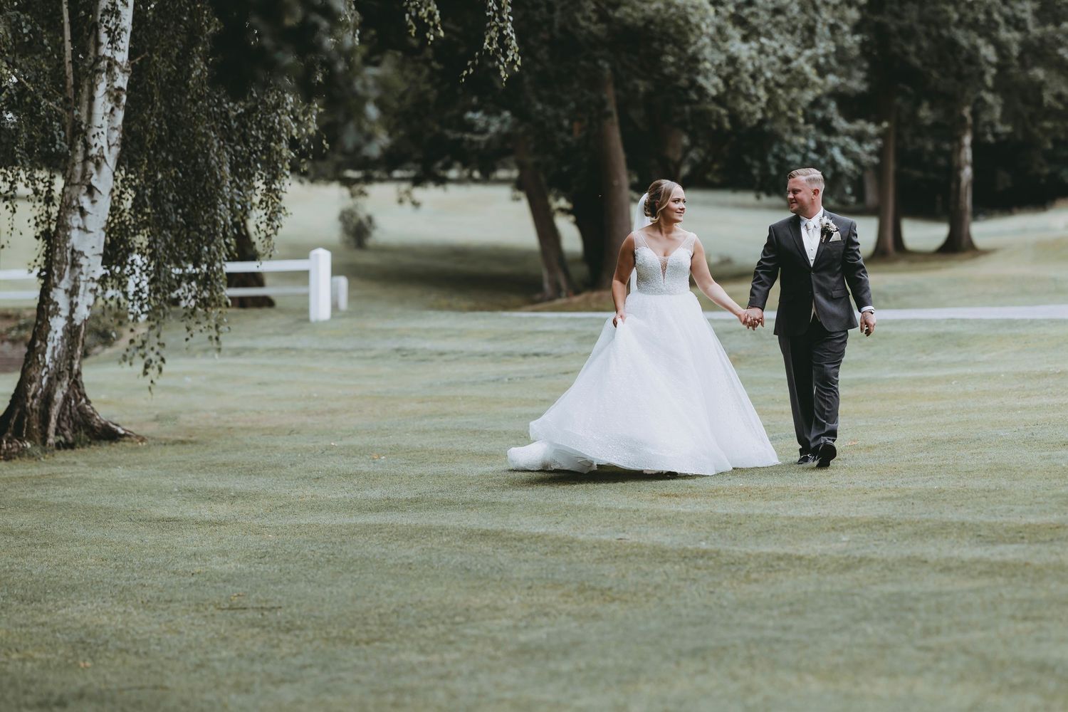Newlyweds sharing an intimate moment while walking on lush grass with trees in the distance at The Warren Estate, Essex.