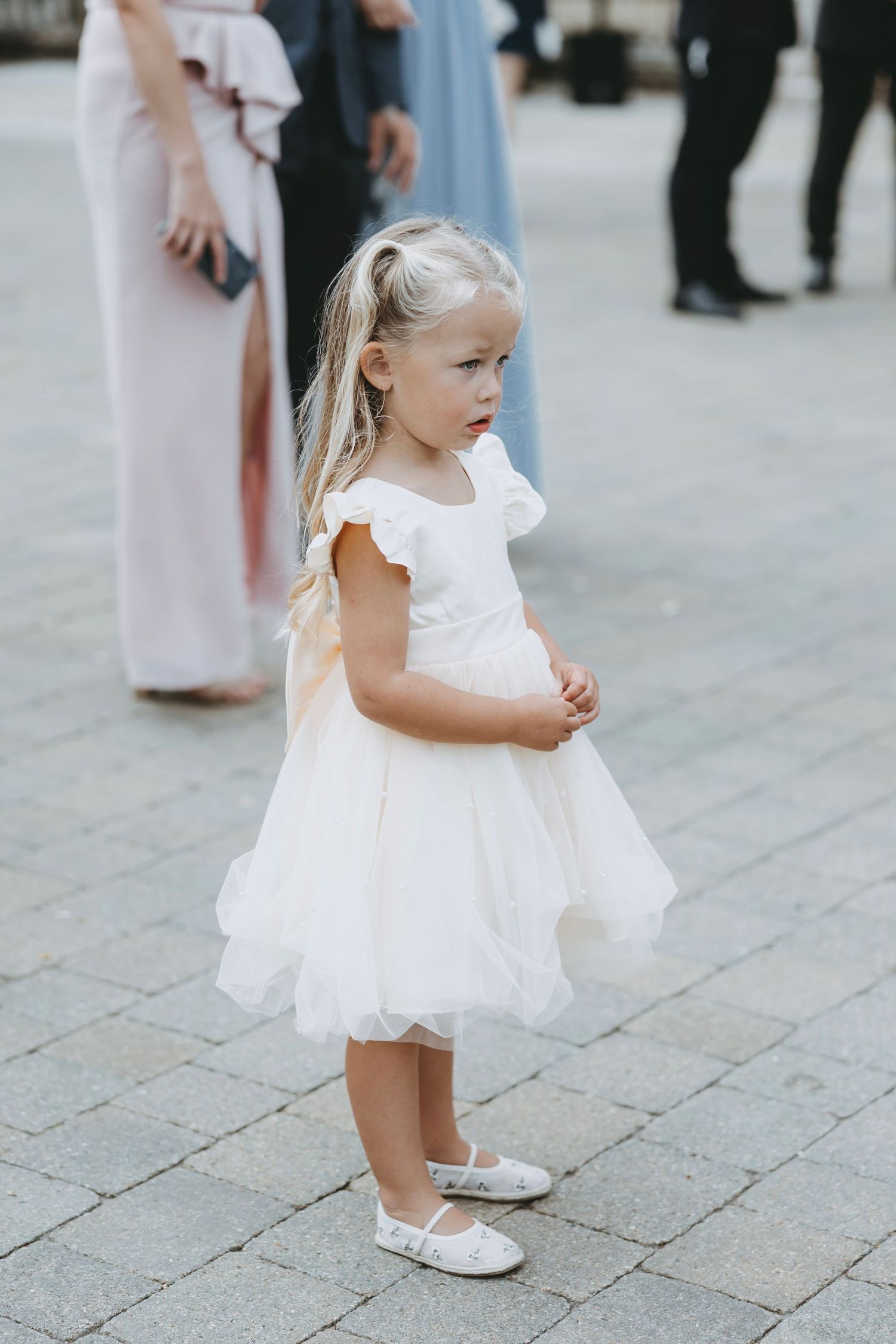 Young flower girl in white dress twirling on stone patio during wedding celebration.