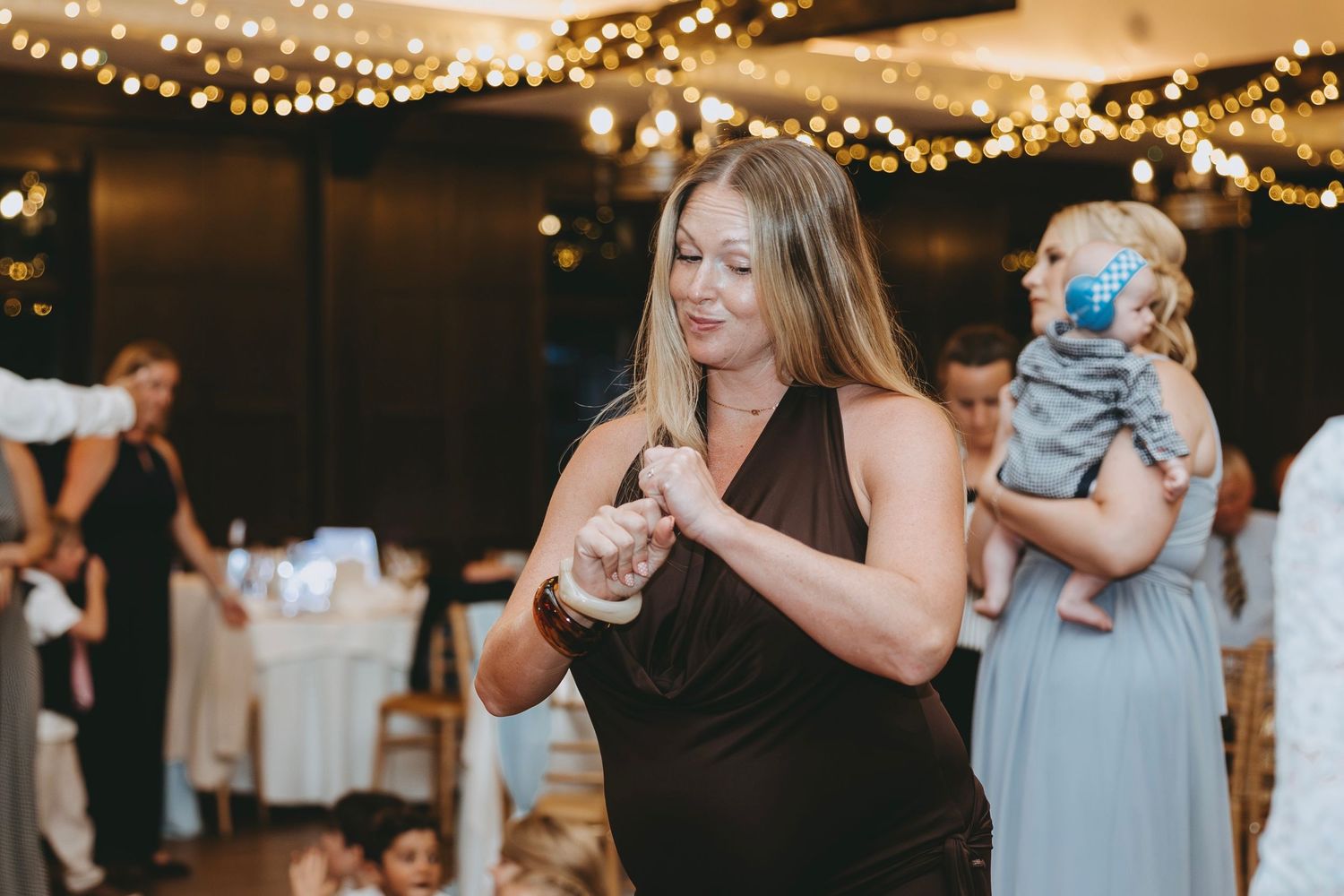 Wedding guests dance beneath warm string lights at an evening reception.