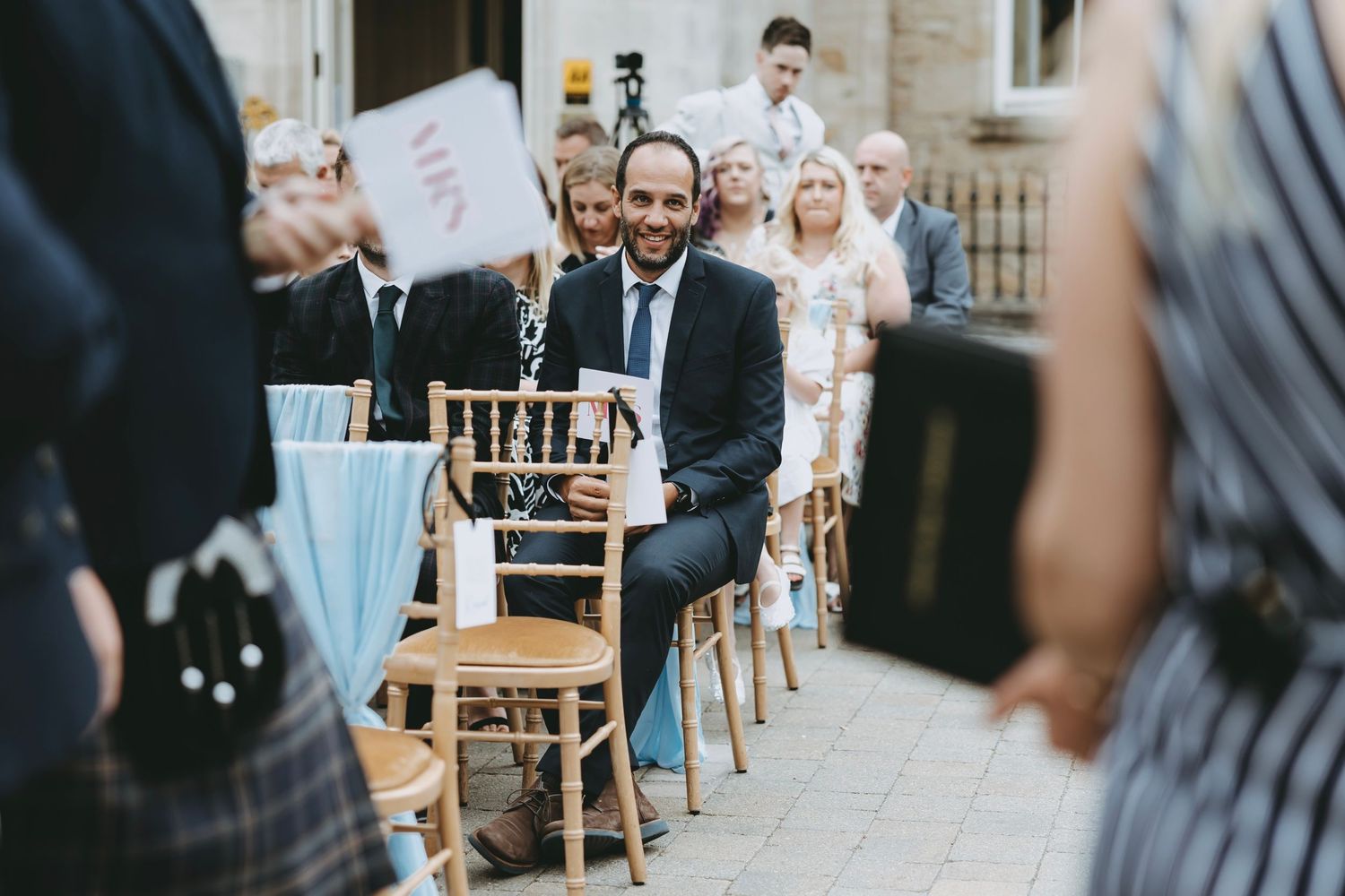 Wedding guests seated in wooden chairs during an outdoor ceremony.