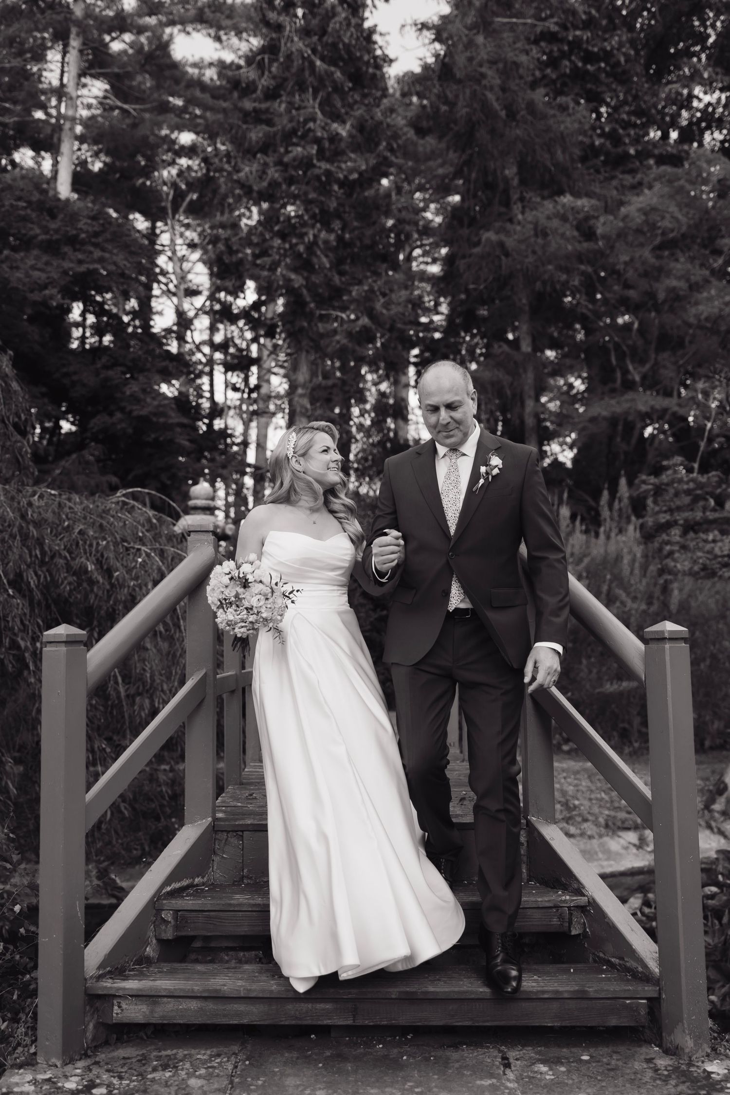 Black and white wedding photos capture playful moments of a couple on a wooden bridge.