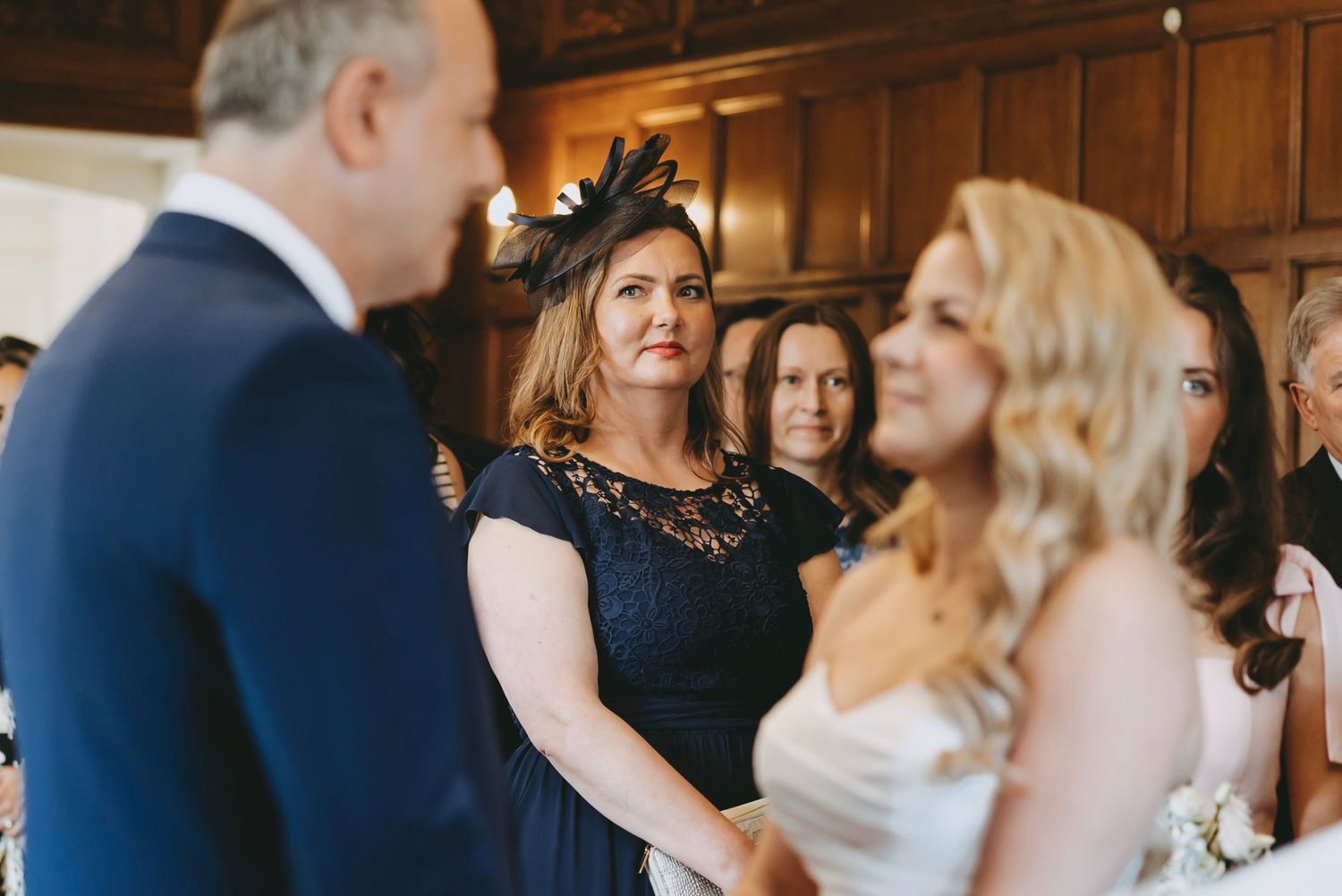 Wedding guests and wedding party gathered in elegant wood-paneled venue during ceremony.