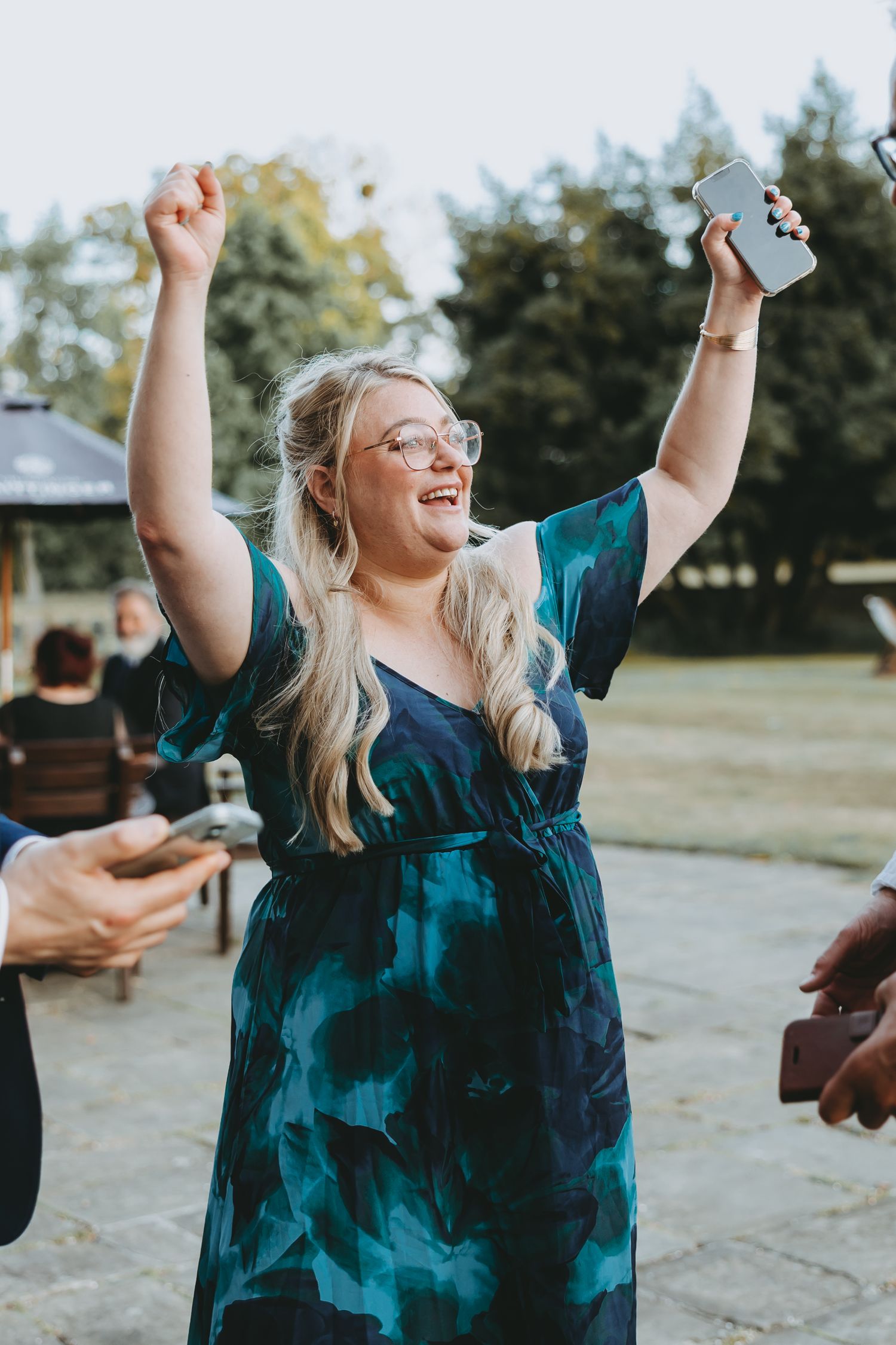 Person in teal dress celebrating joyfully with raised arms during an outdoor event.