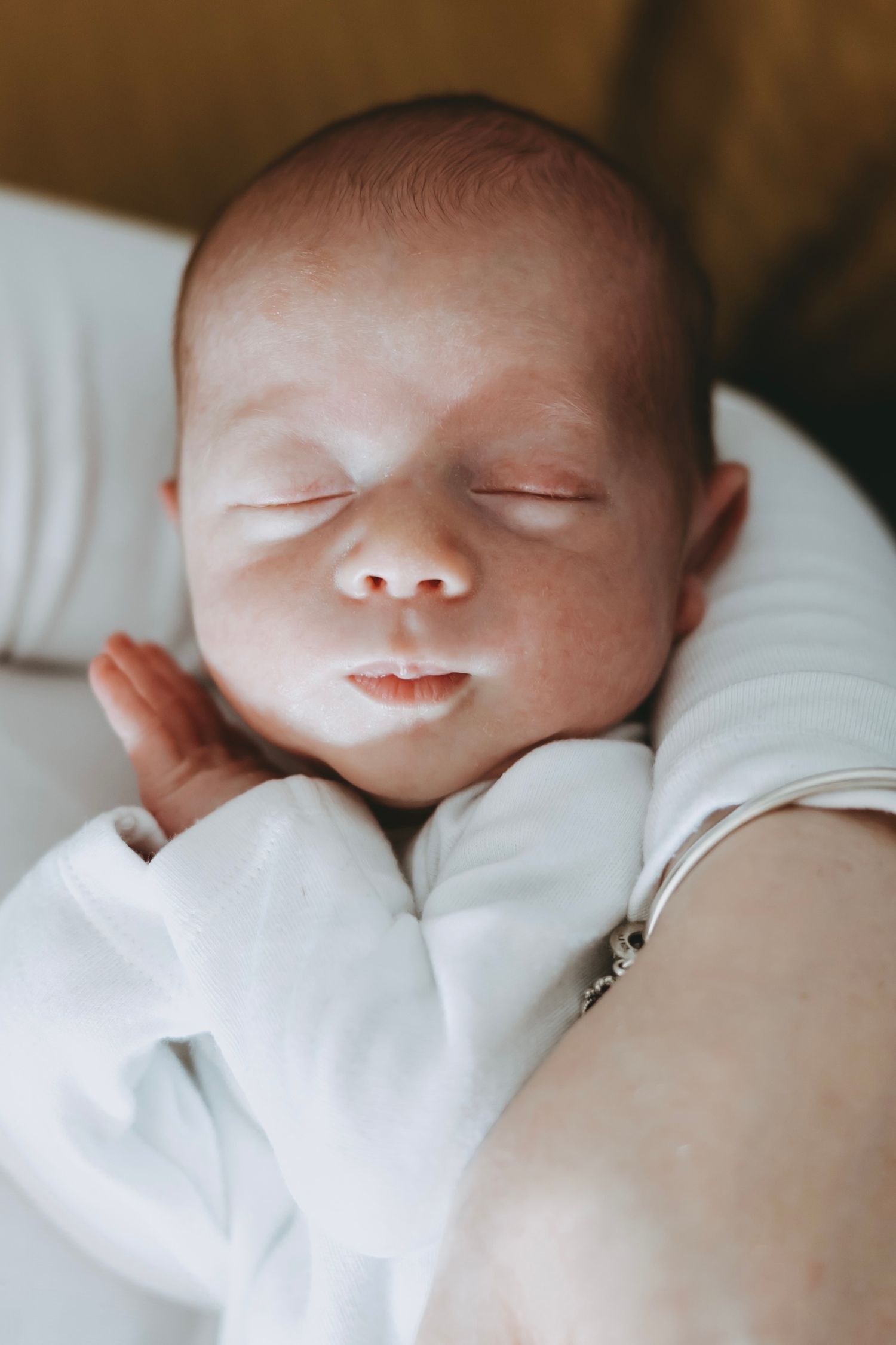 A sleeping newborn baby in white clothing rests peacefully on soft white bedding.