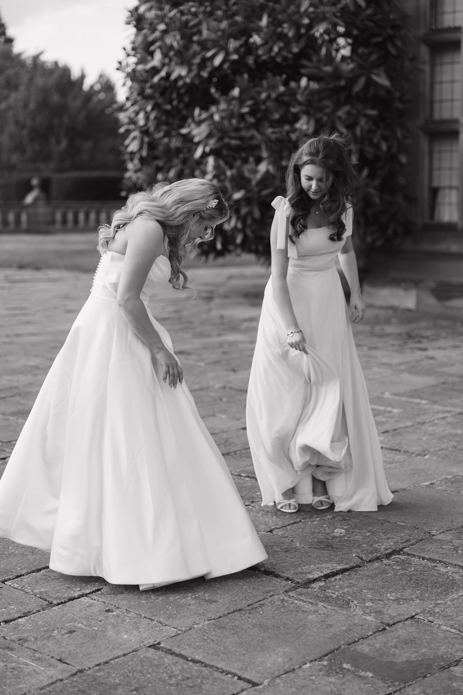 Two people in white dresses examine details on the stone patio during a wedding at Fanhams Hall, Ware, Hertfordshire.