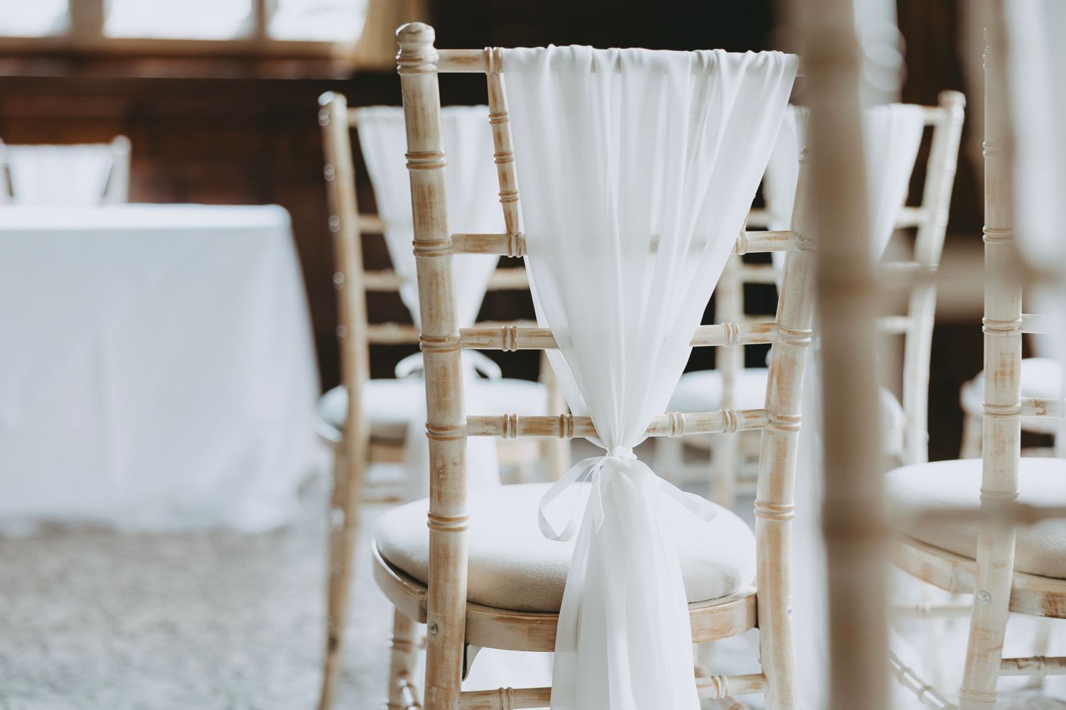 White fabric sashes tied elegantly on wooden ceremony chairs in a row.