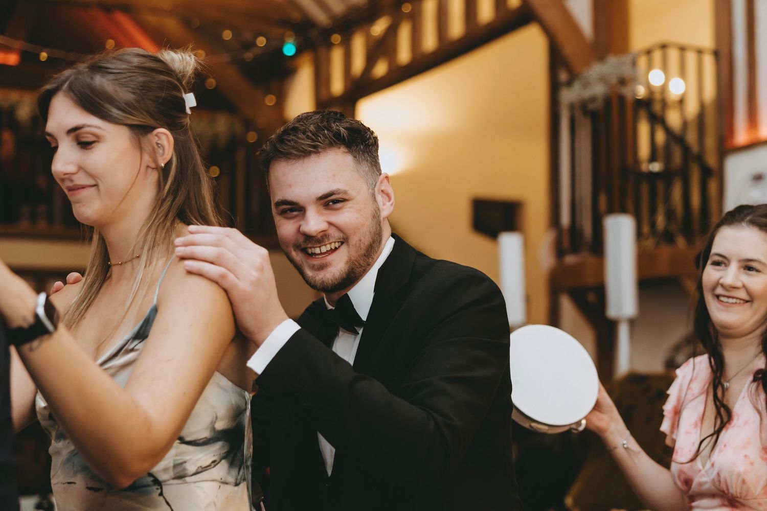 Reception guests enjoying dance floor moments at rustic venue with wooden beams.