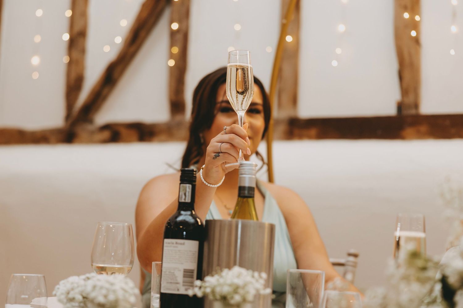 Wedding reception table settings with wine glasses and floral centerpieces under wooden beams.