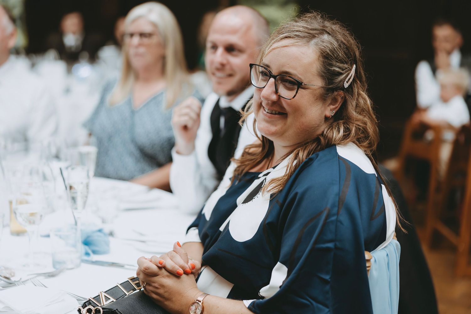 Wedding guests seated at a reception table with wine glasses and place settings.