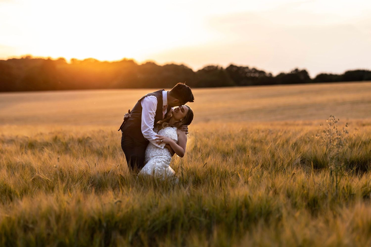 Romantic couple embracing in golden wheat field at sunset at Shenley Manor, Hertfordshire.