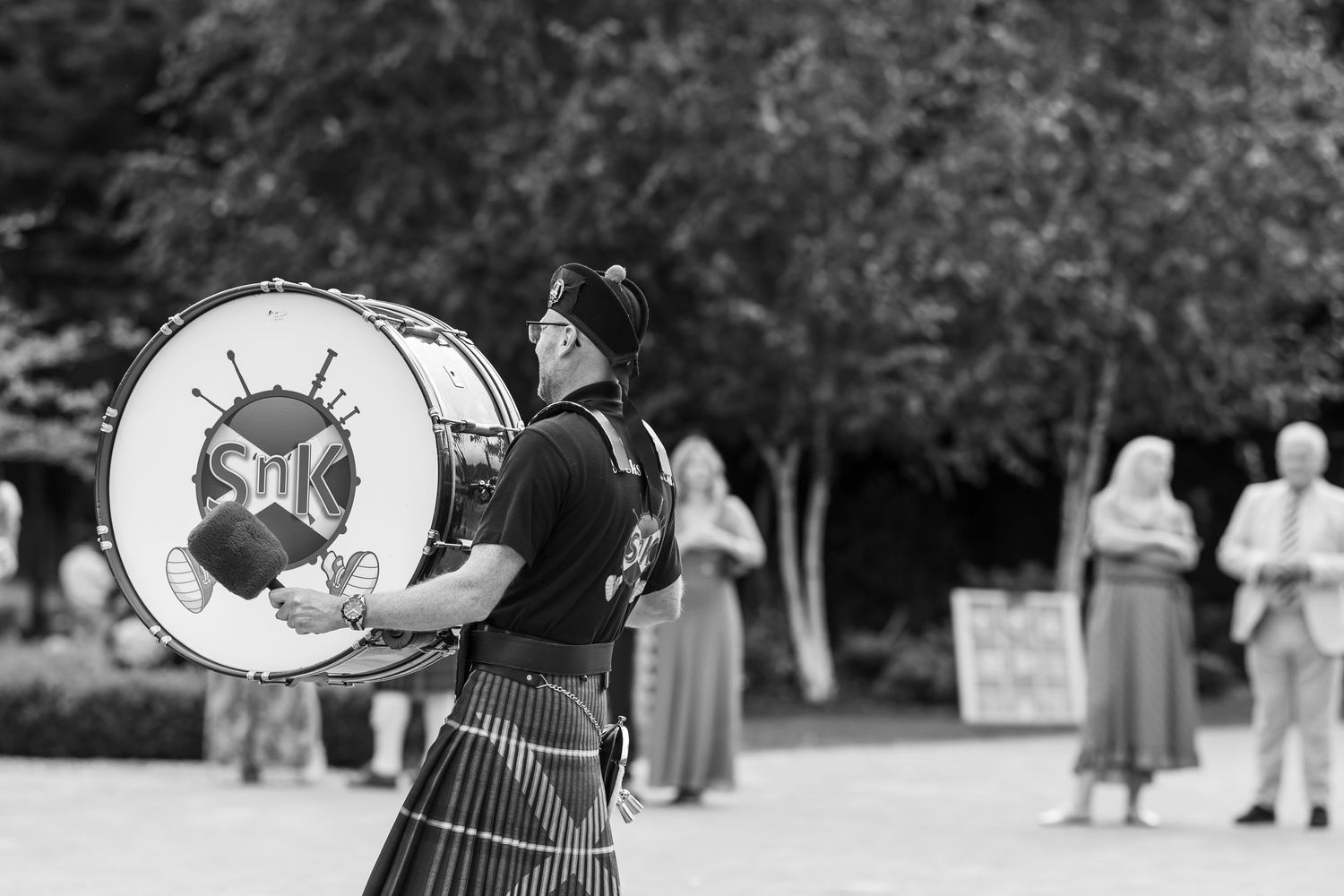 Scottish drummer in traditional kilt performs with a large bass drum at an outdoor event.