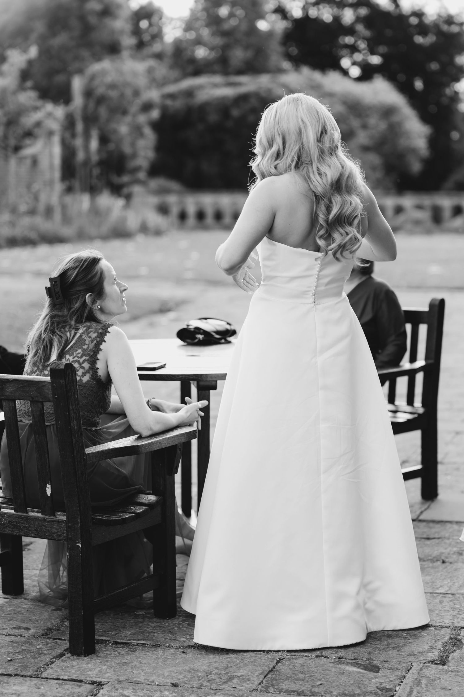 Black and white photo showing elegant white wedding dress details on a stone patio at Fanhams Hall, Ware, Hertfordshire.