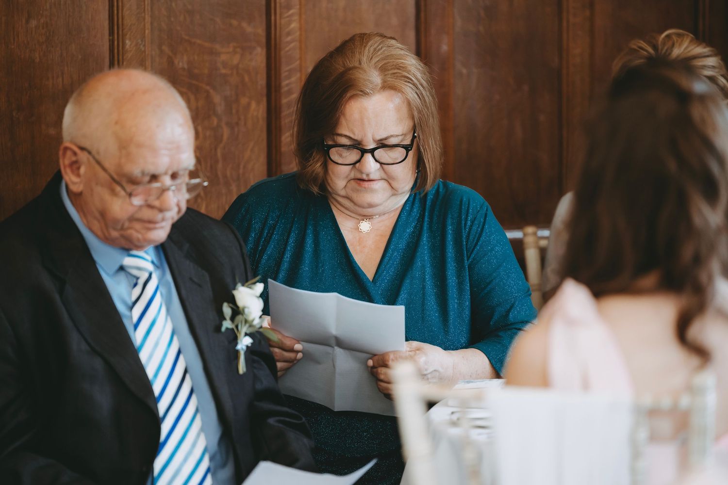 Guests at formal event reviewing papers at wooden-paneled banquet table.