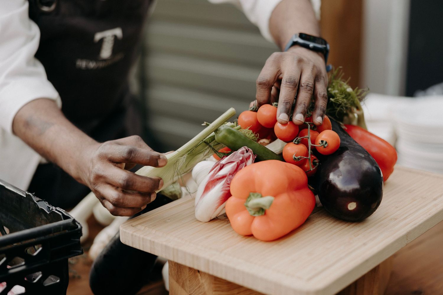 Chef chopping fresh vegetables on wooden cutting board in professional kitchen.