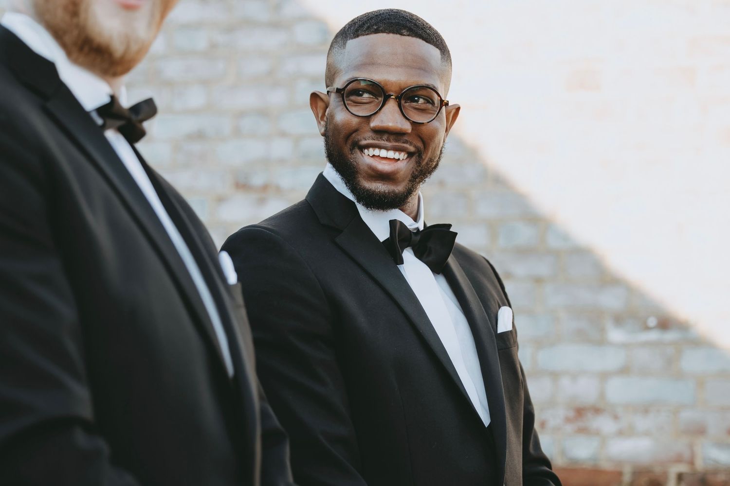 A person in a black tuxedo and bow tie smiles during a formal event.
